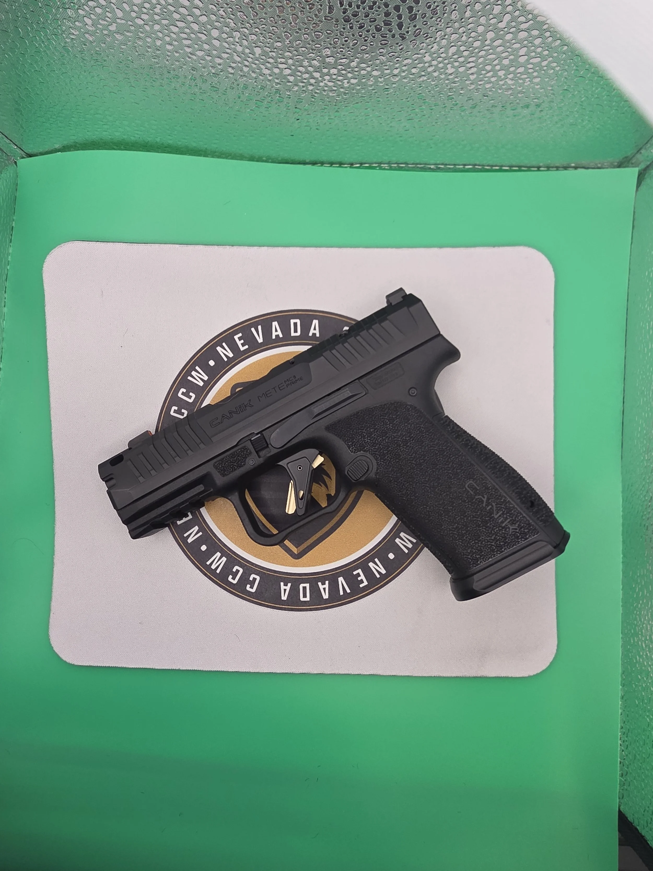 A black handgun resting on a Nevada-themed paper inside a green storage container.