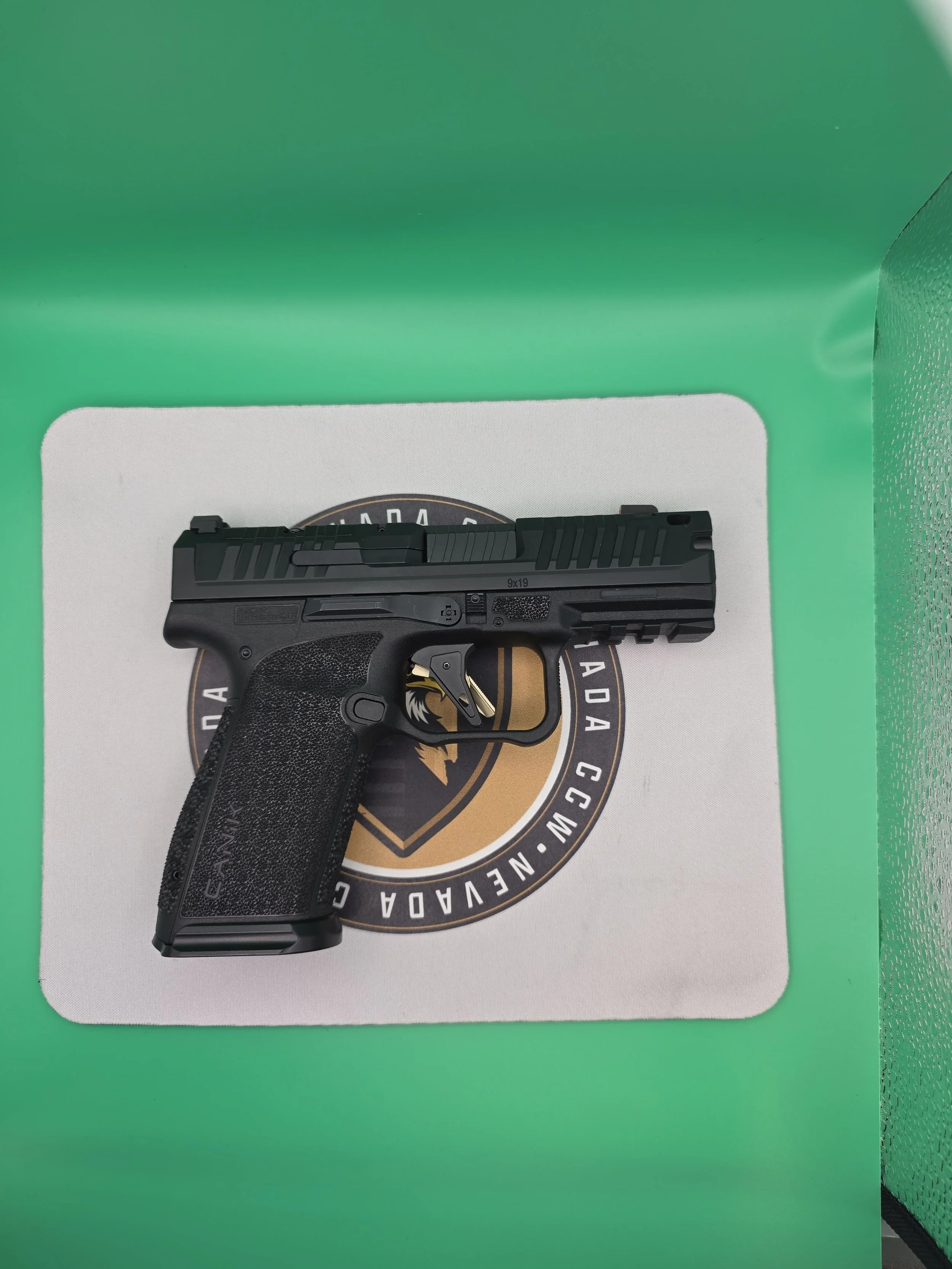 A black handgun on top of a white item with a circular logo, placed on a green surface.
