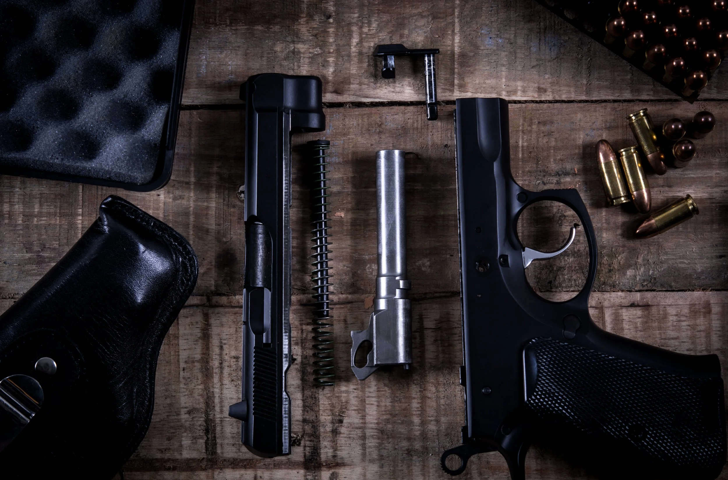 A wooden table with handgun parts, bullets, and a black leather holster.