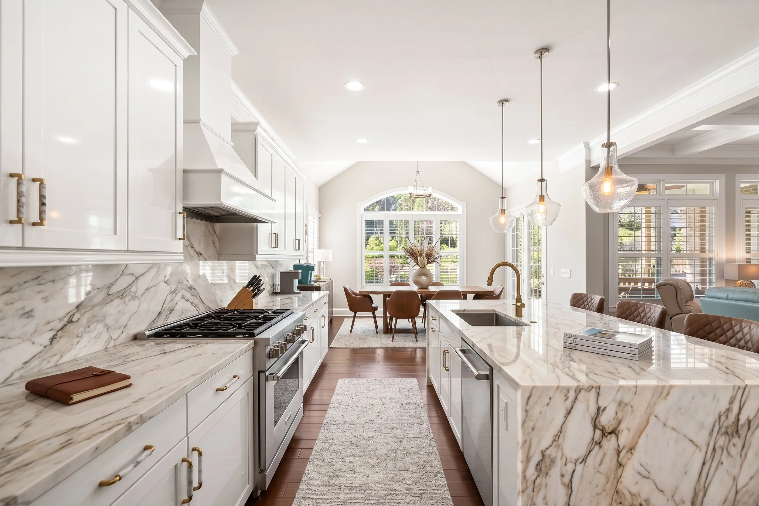 Modern kitchen with white cabinets, marble countertops, pendant lights, and a dining area with a large window.