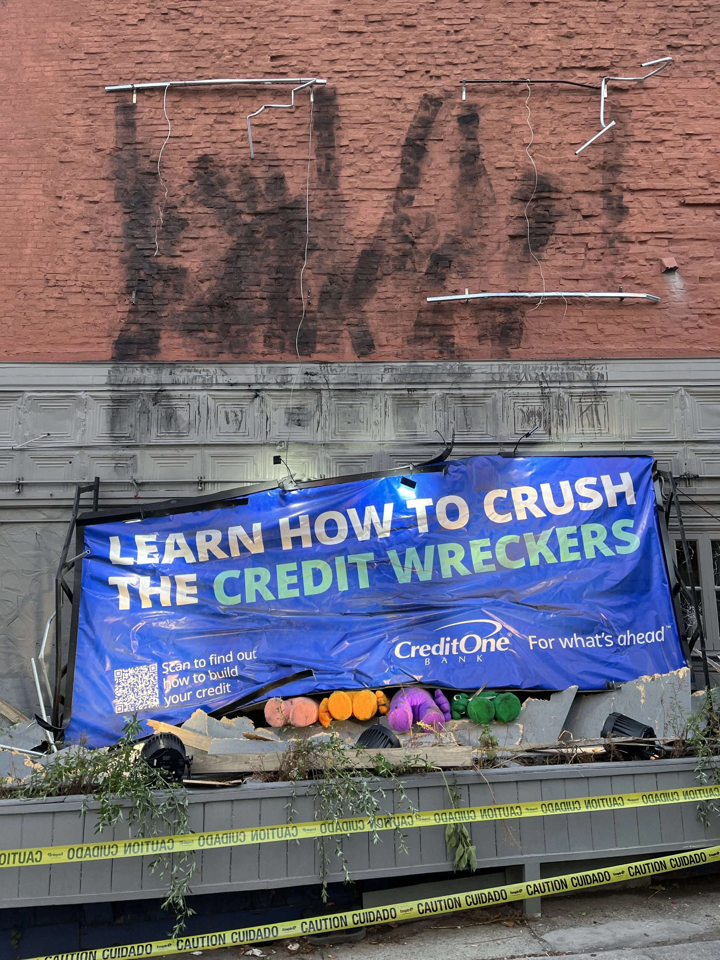Protest or demonstration scene with a banner that promotes learning how to improve credit scores, supported by a scaffolding structure with caution tape around it. Items such as colorful pumpkins or pumpkins-like decorations are at the bottom of the 