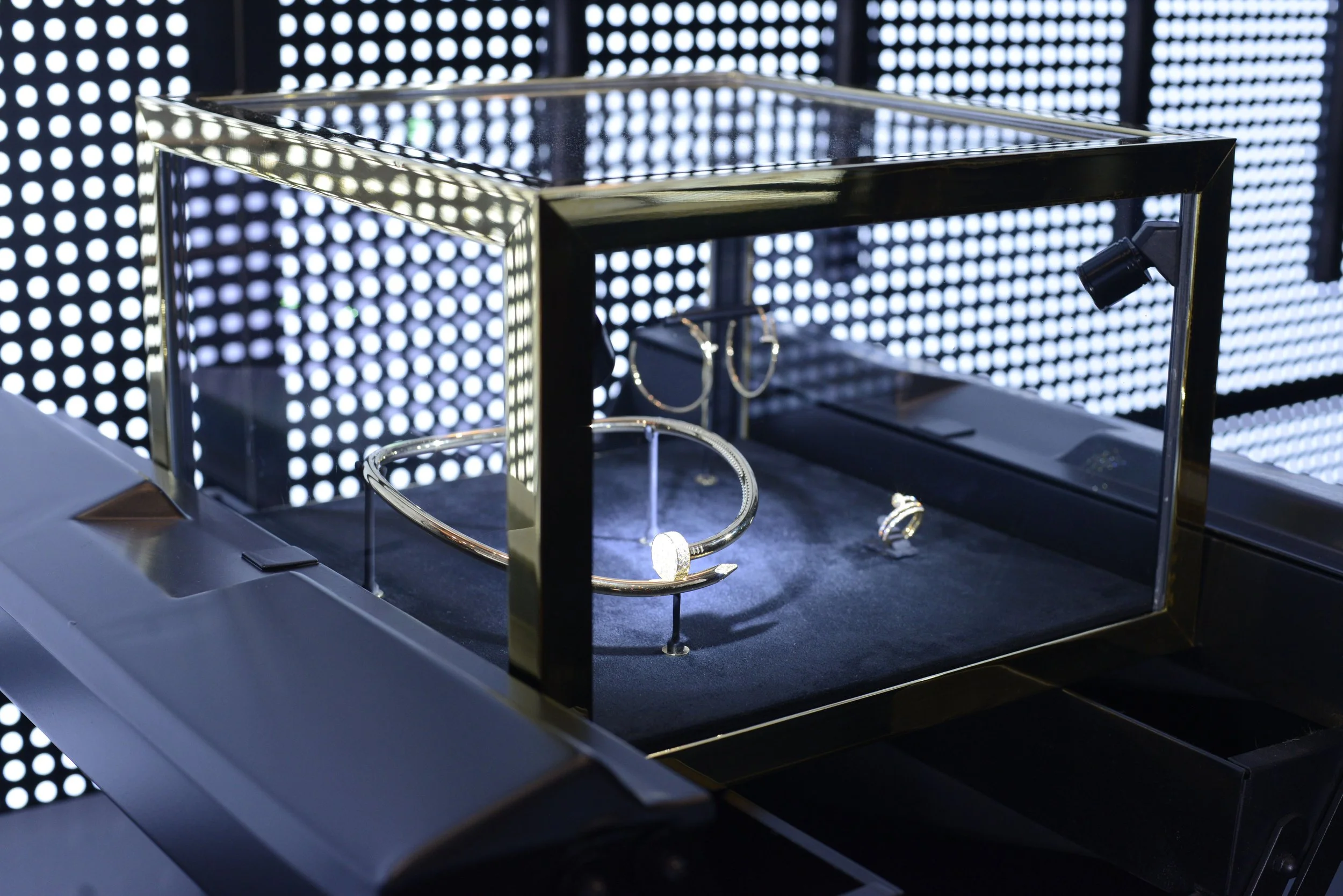 Display case with jewelry, including rings and bracelets, in front of a black backdrop with bright circular lights.