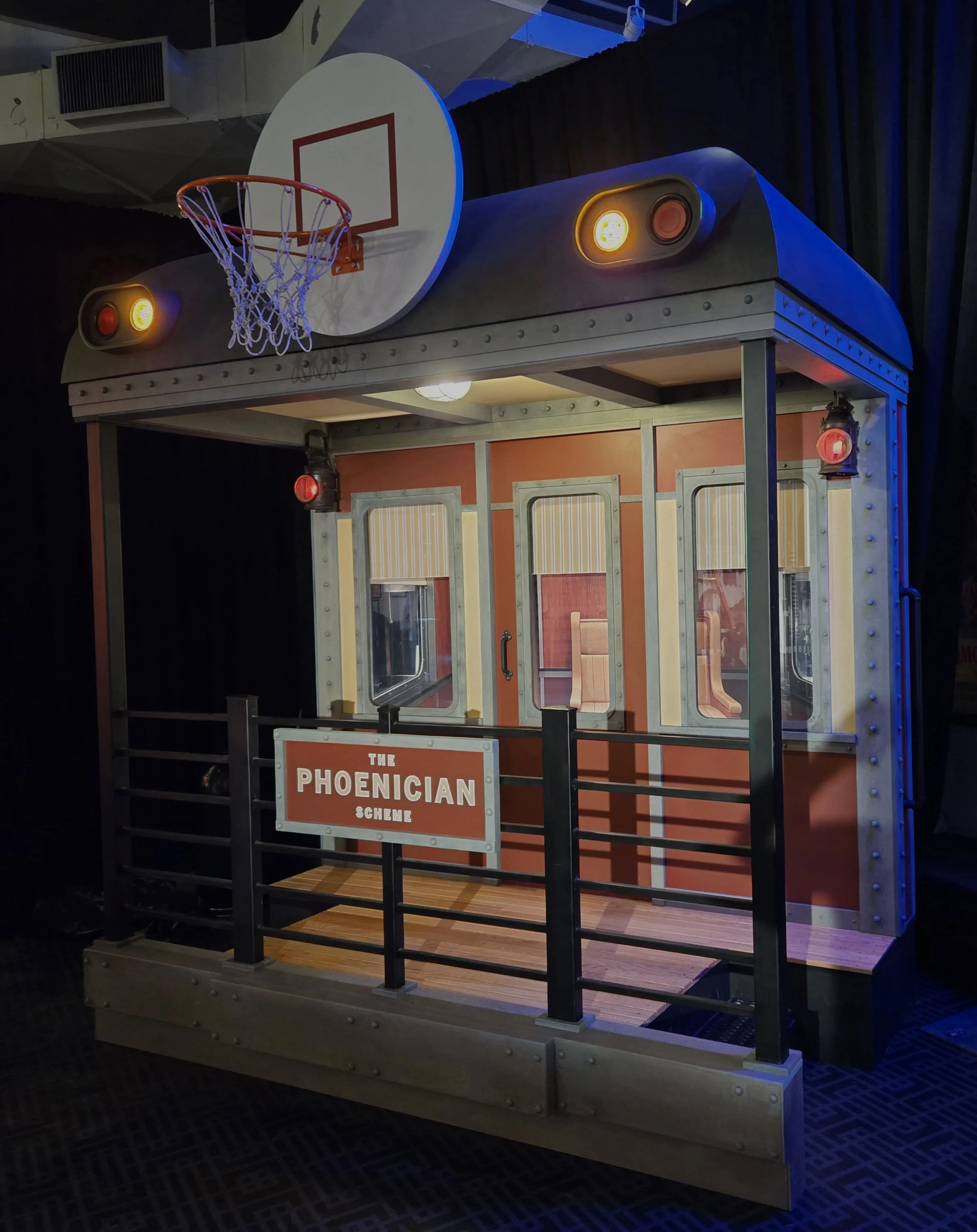 A miniature indoor basketball court with a hoop and backboard, part of an exhibit called 'The Phoenician Scheme'.