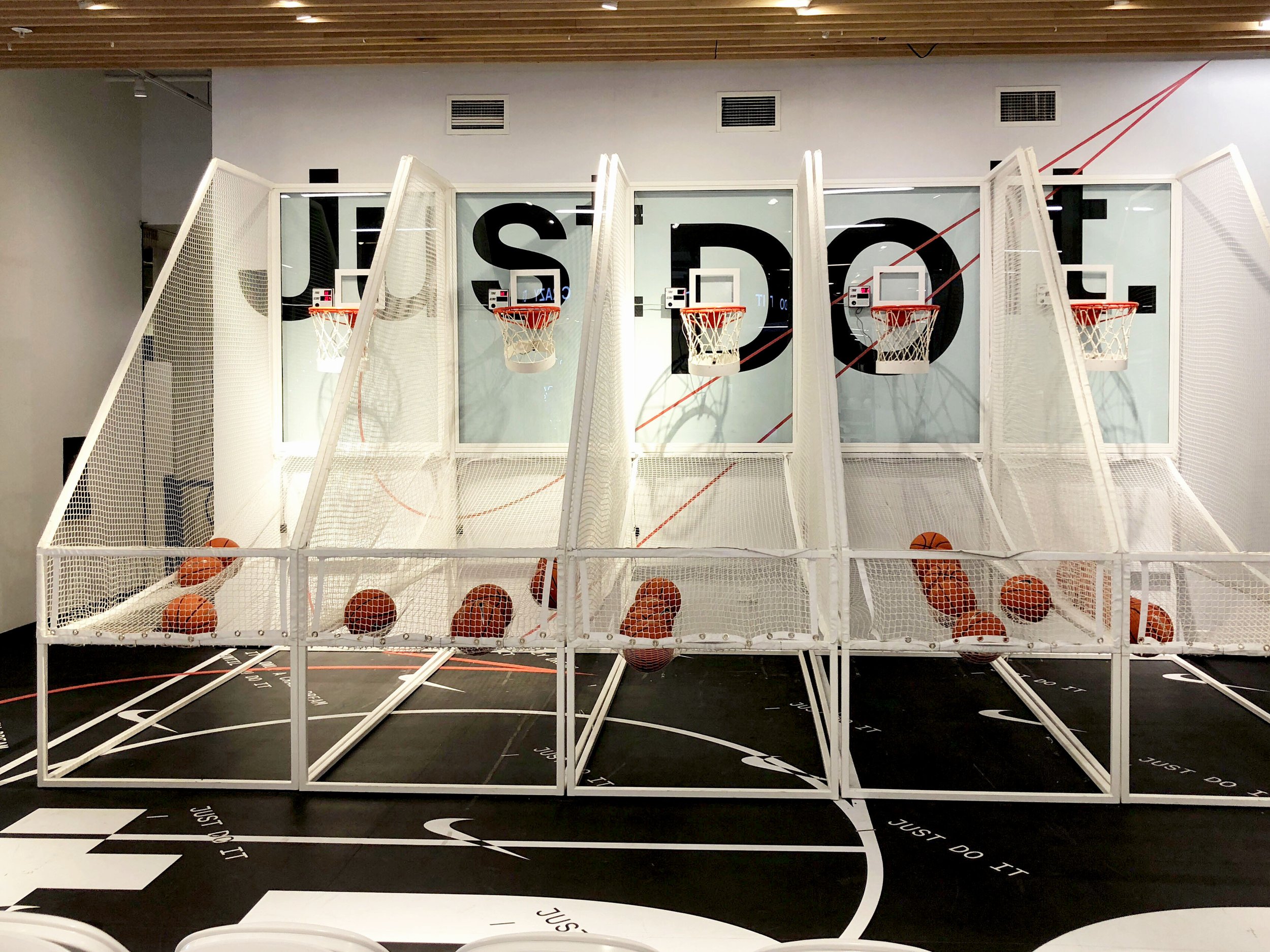 A miniature basketball court with three small basketball hoops and basketballs inside a white protective net, set up in an indoor space.