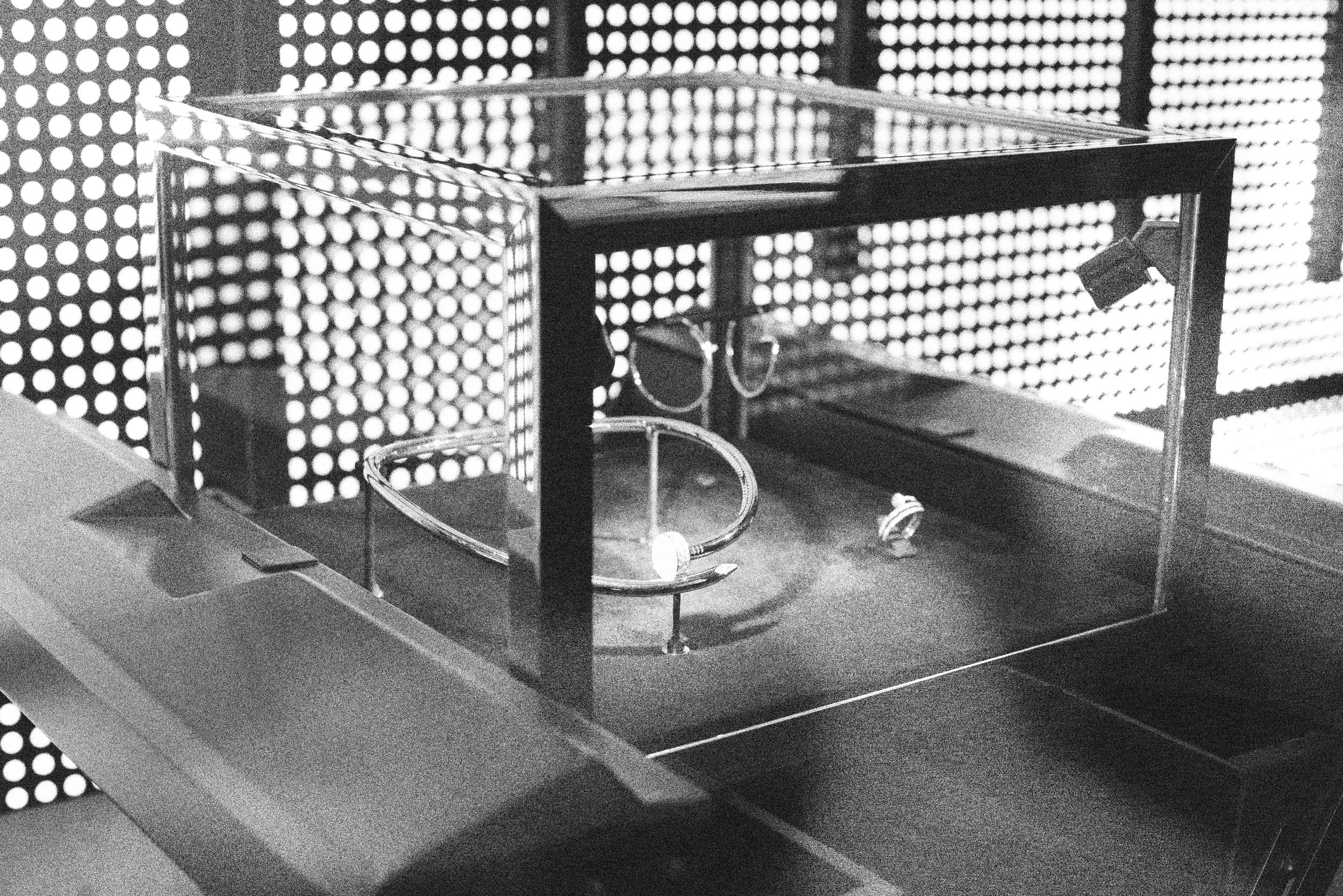 Black and white photograph of scientific laboratory equipment, including a microscope, placed on a table with a backdrop of illuminated perforated panels.