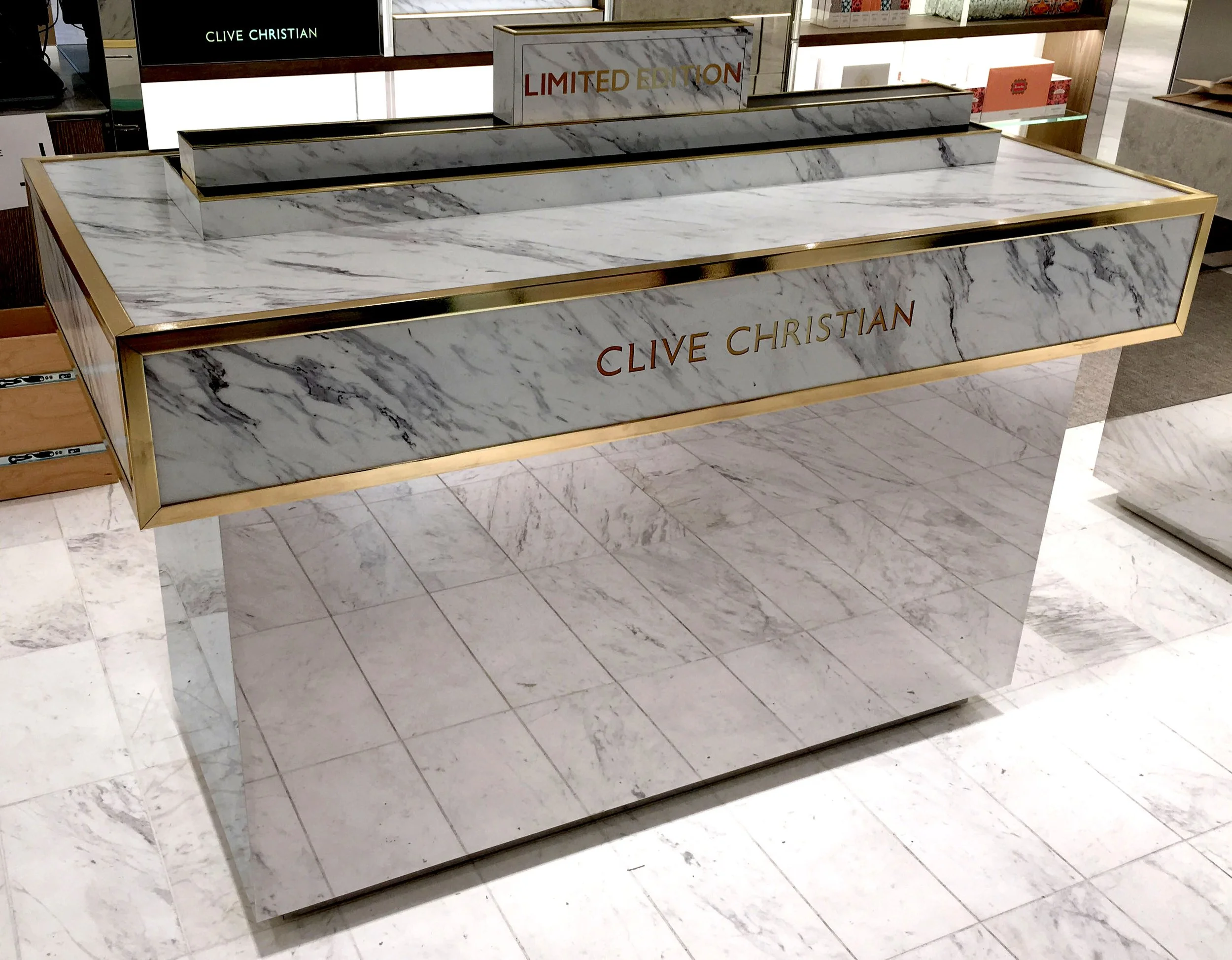 Marble display table with gold trim at Clive Christian store, featuring signs for 'Limited Edition' and 'Clive Christian' branding.