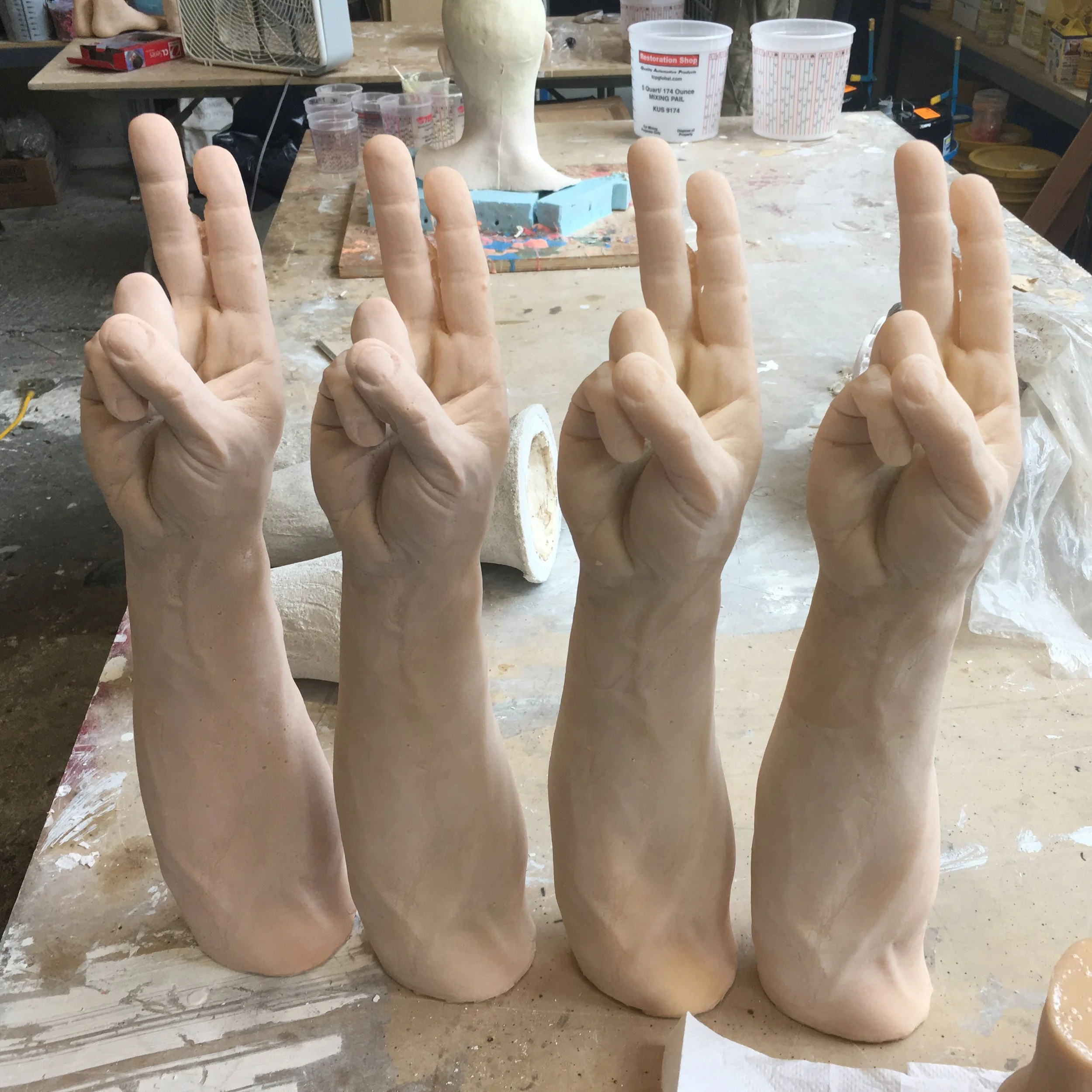 Several unfinished, life-sized clay sculptures of hands with fingers pointing upwards on a worktable in a ceramics or sculpture studio.