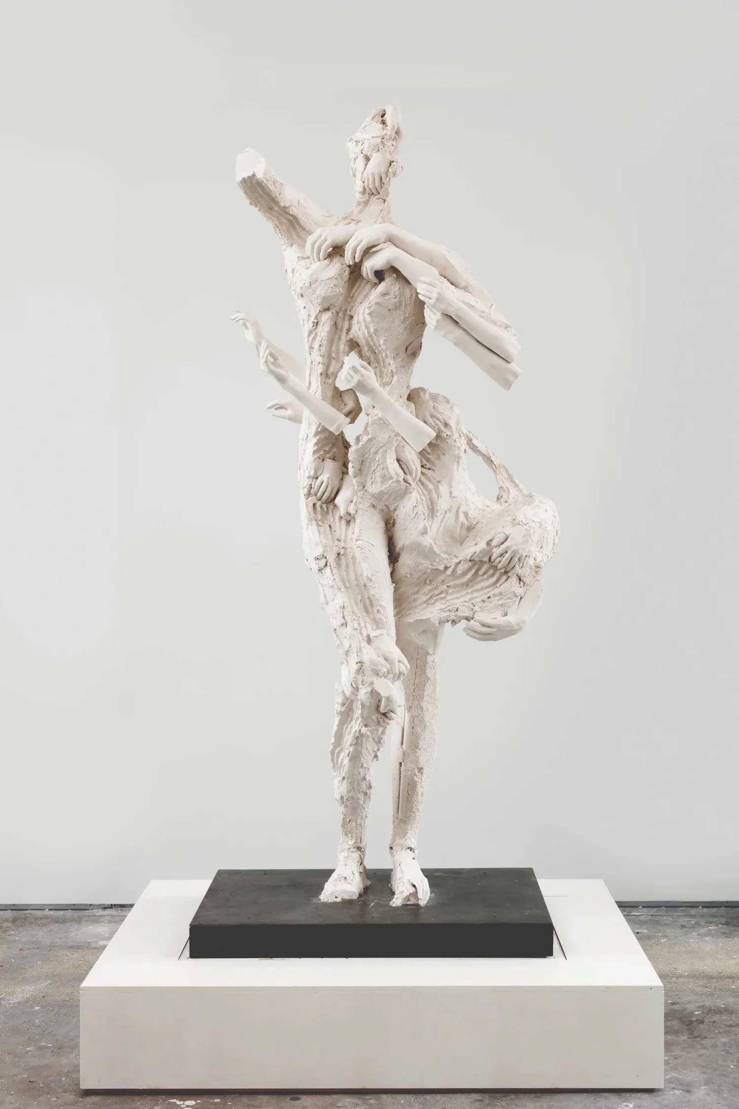 A white sculpture of a figure with several arms and a lion's body, standing on a black base with a white surrounding platform.