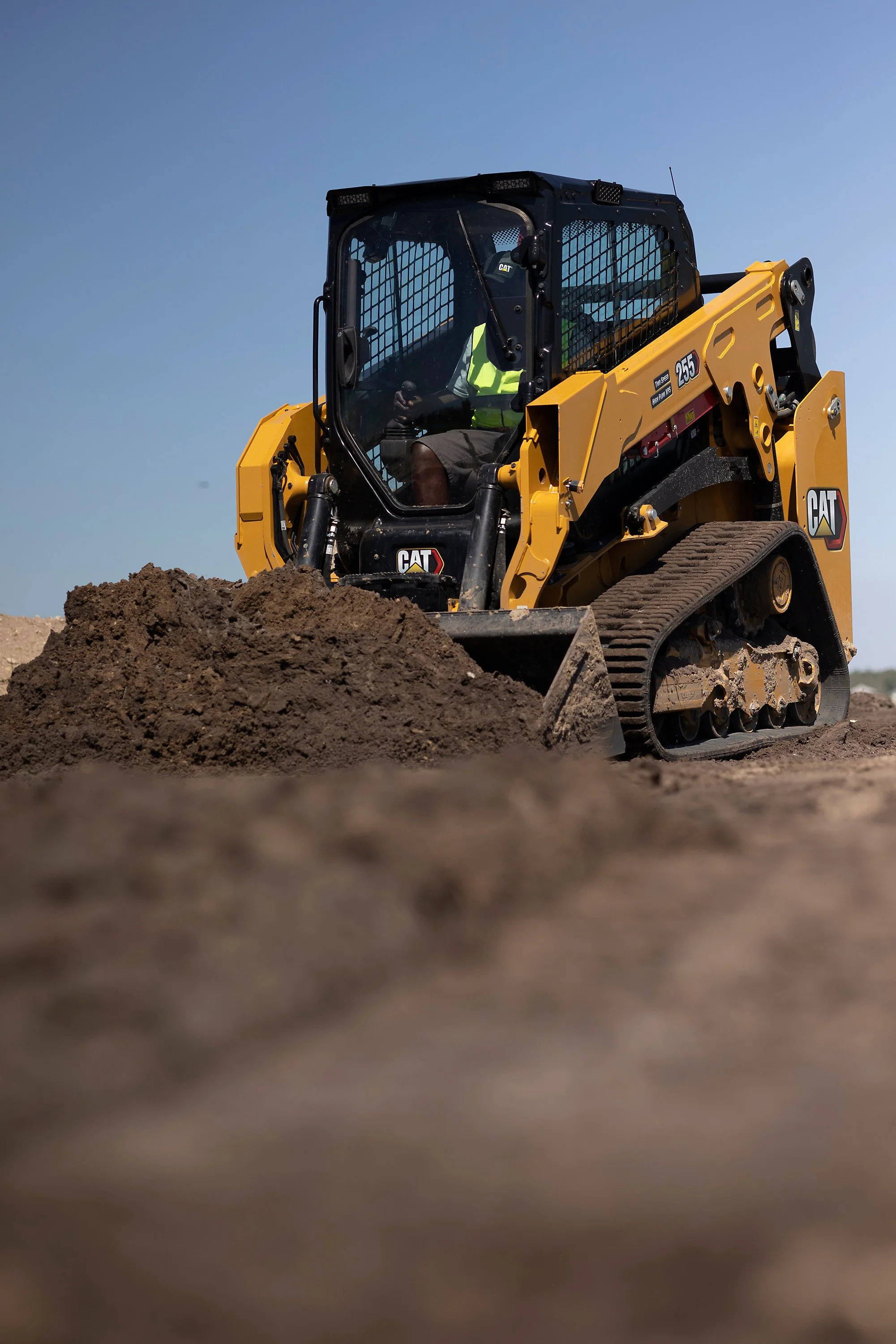 A yellow CAT skid steer loader operating on dirt against a clear blue sky.