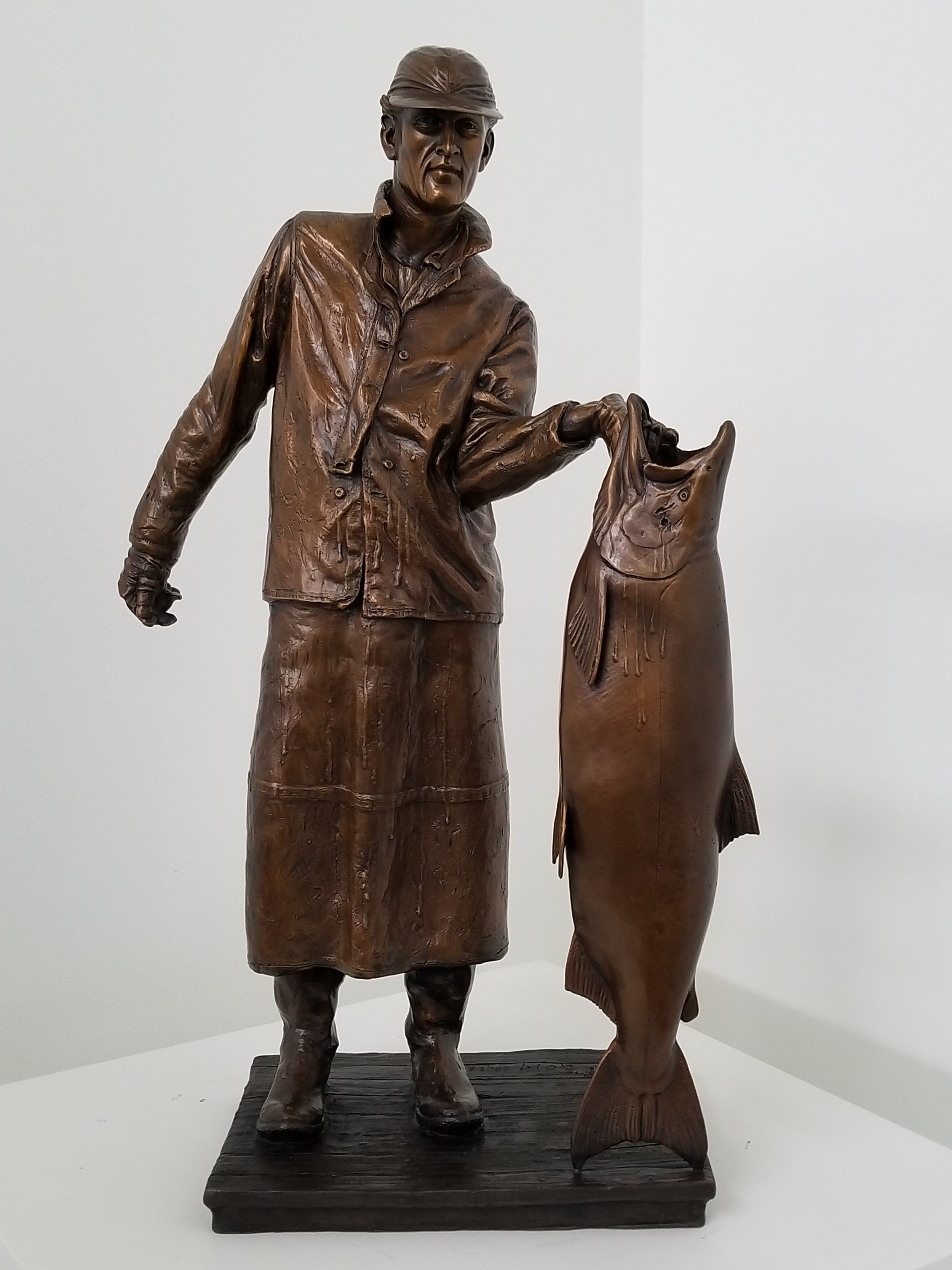 Bronze sculpture of a man in fishing attire holding a large fish.