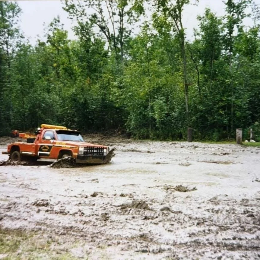 An orange rescue vehicle partially submerged in a flooded area with muddy water, surrounded by green trees.