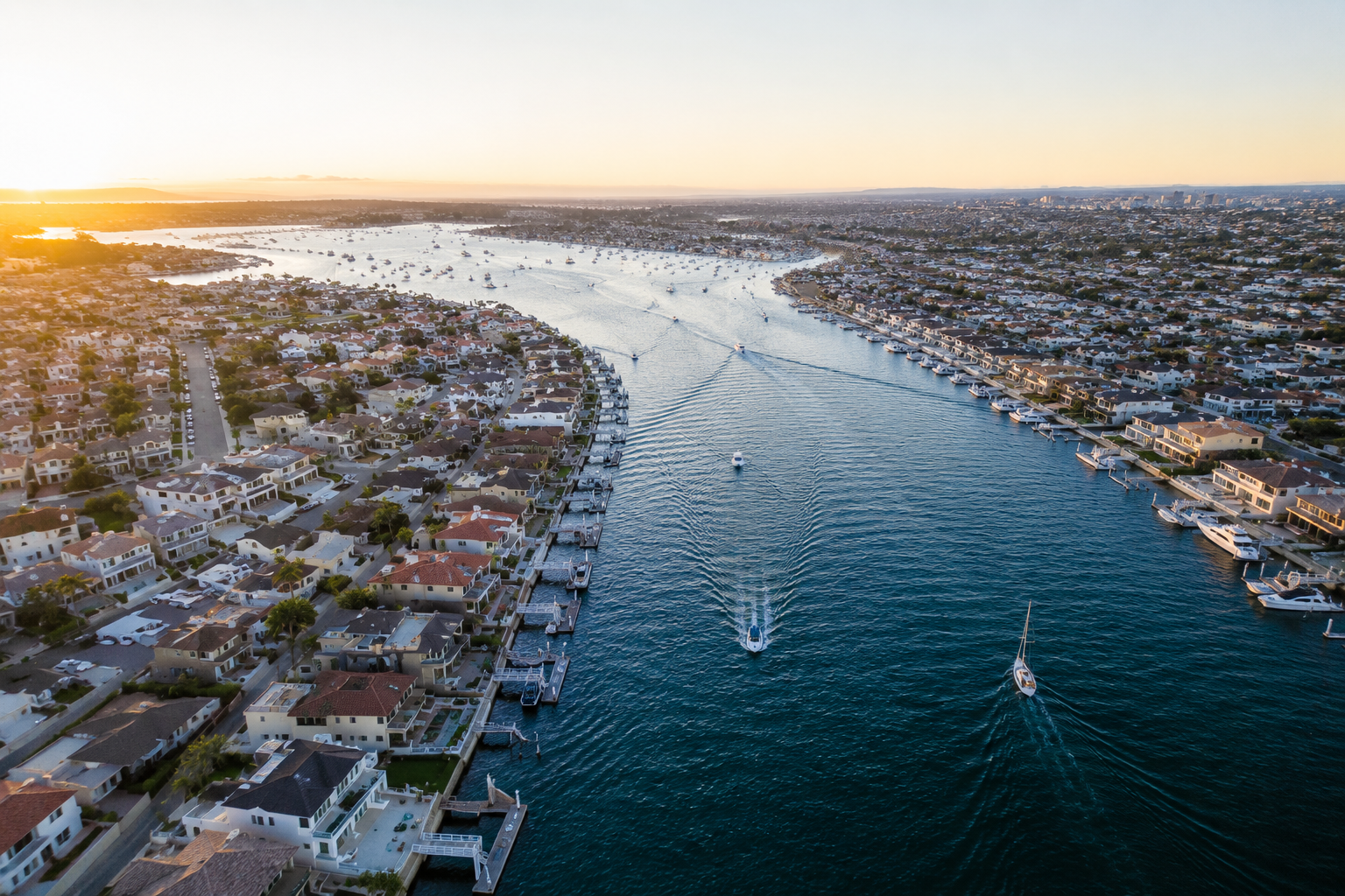 Aerial view of a residential neighborhood along a river at sunset with boats moving through the water.