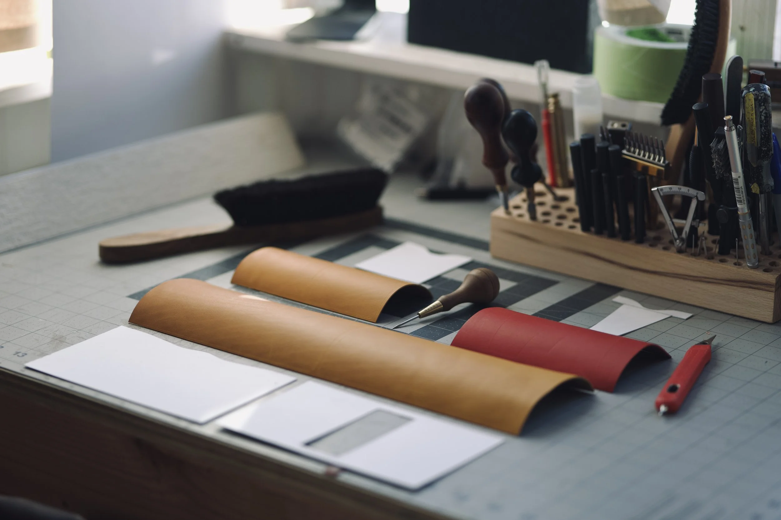 A work surface with leather swatches, a marking pen, and other tools, with organized tools and supplies in the background.