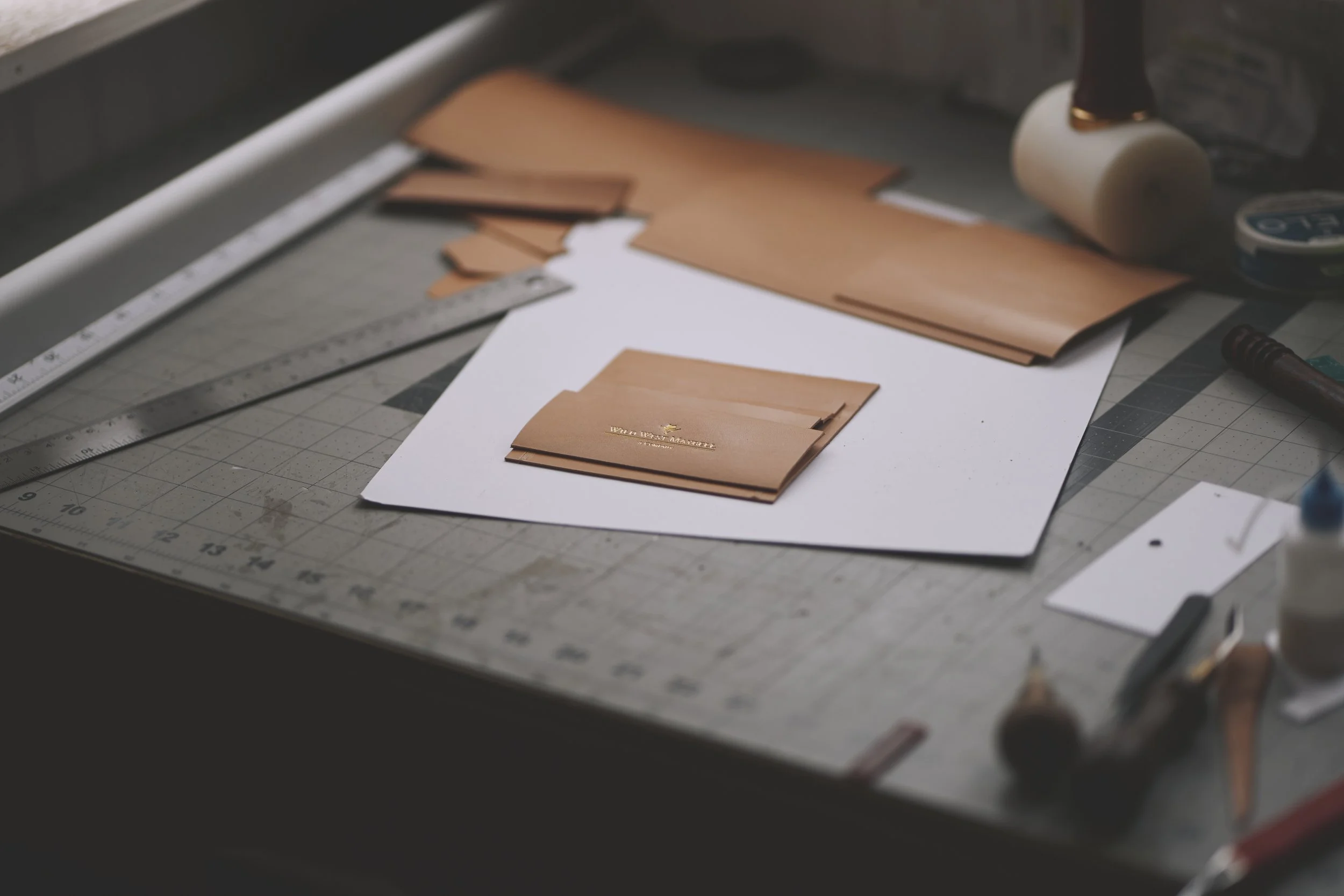 Leather sample swatches and tools on a cutting mat in a workshop.
