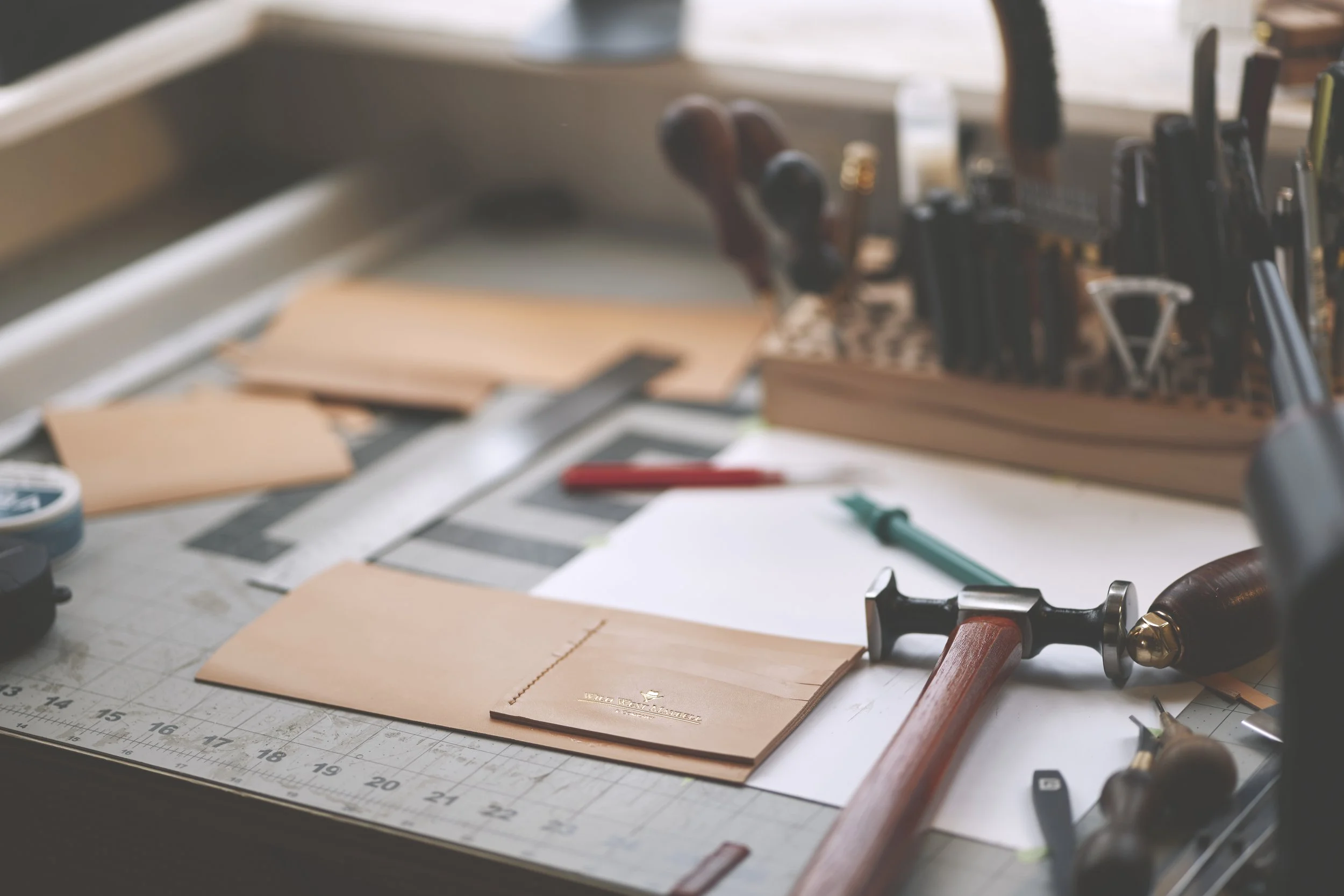 A cluttered workbench with tools like a hammer and screwdriver, and pieces of cardboard or paper on a cutting mat.