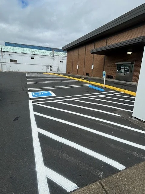 Empty parking lot with designated handicapped parking space and sloped lines for accessible parking near a brick building under a cloudy sky.