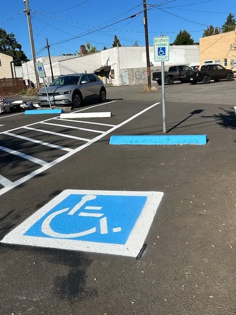 Parking lot with handicapped spaces, including a designated accessible parking spot with a blue and white wheelchair symbol painted on the ground, and a sign indicating reserved parking for handicapped individuals.
