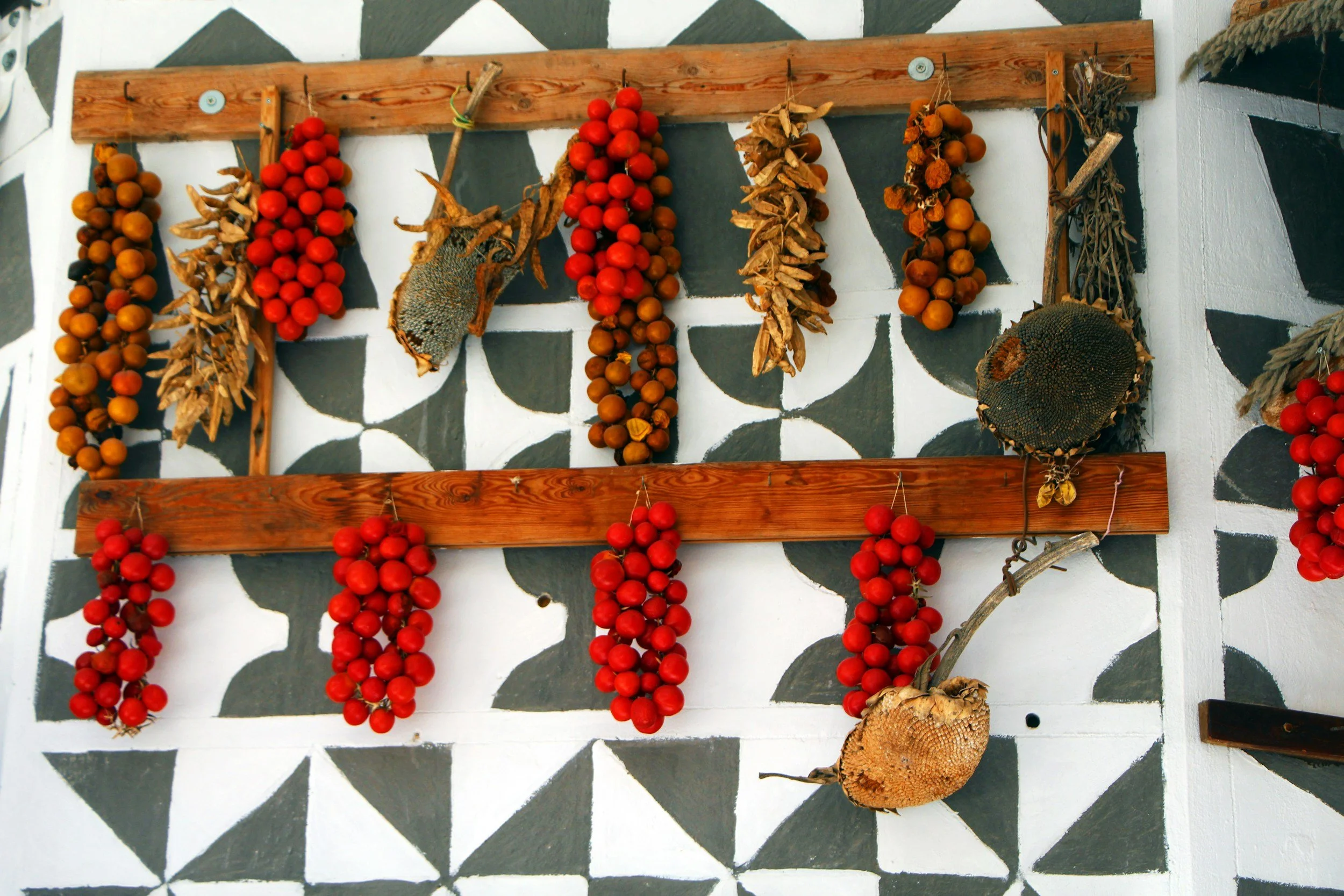 Bundles of red, orange, and brown dried berries hanging on a wooden rack against a black and white patterned wall.