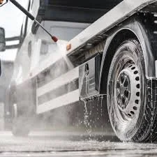 Person pressure washing a vehicle outdoors, water and soap spraying on the tire and side