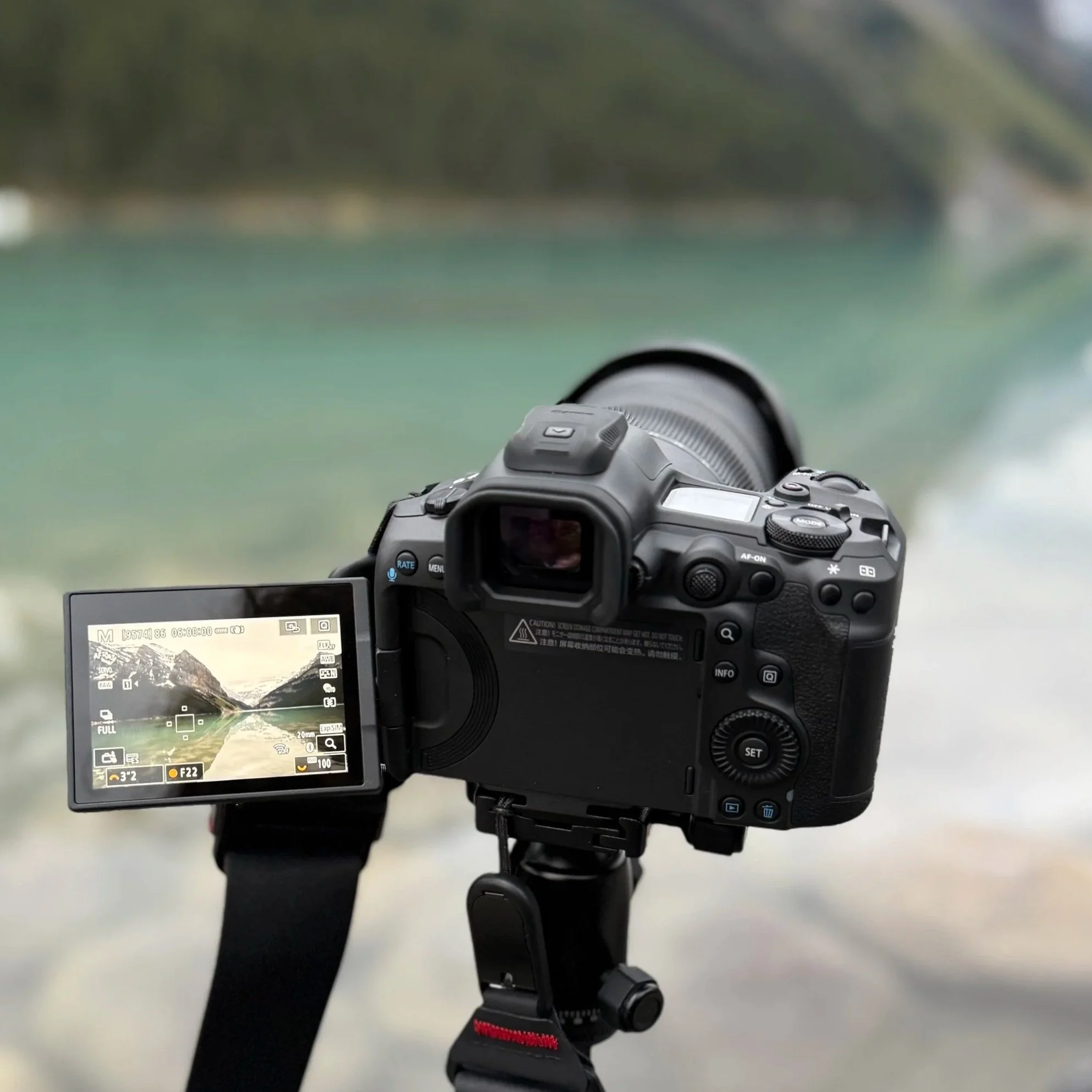 Digital camera mounted on a tripod, focused on a water body with trees in the background.