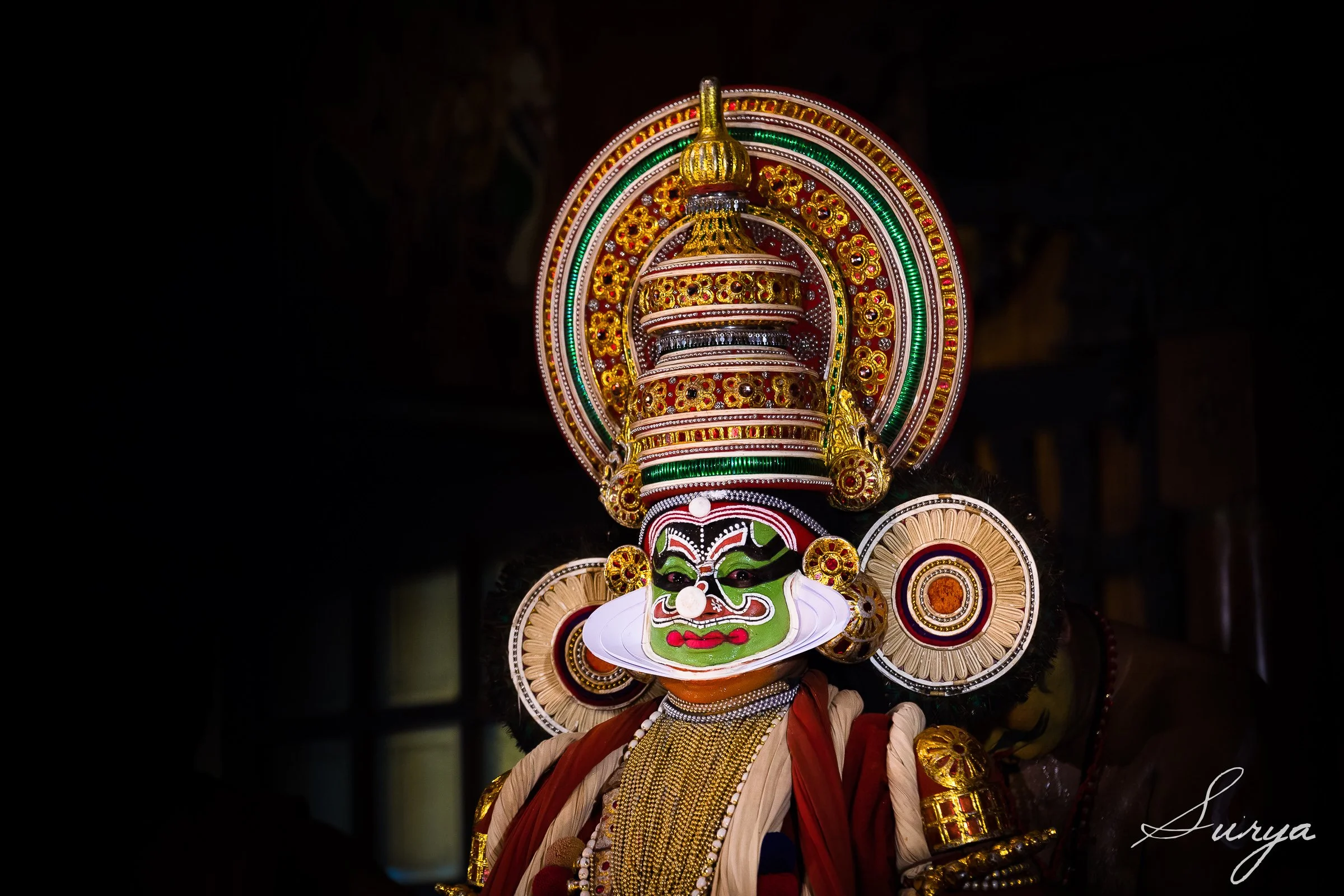 A traditional Kathakali dancer wearing elaborate, colorful costume and face paint during a performance at night.