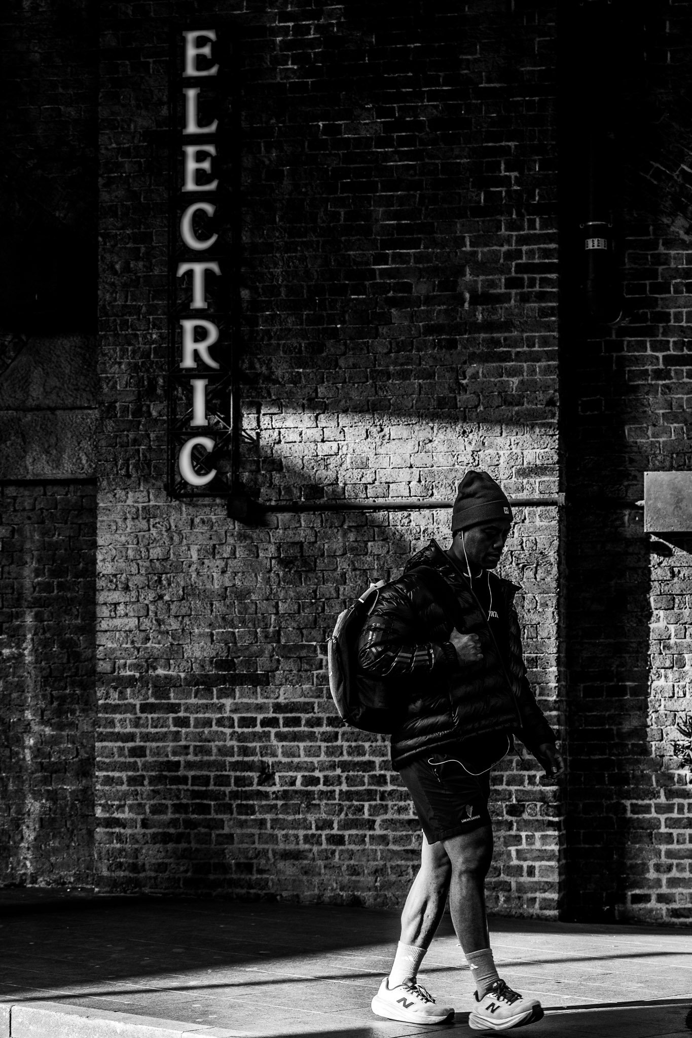 Man in sportkleding tijdens het hardlopen op straat bij nacht, met een bakstenen muur op de achtergrond.