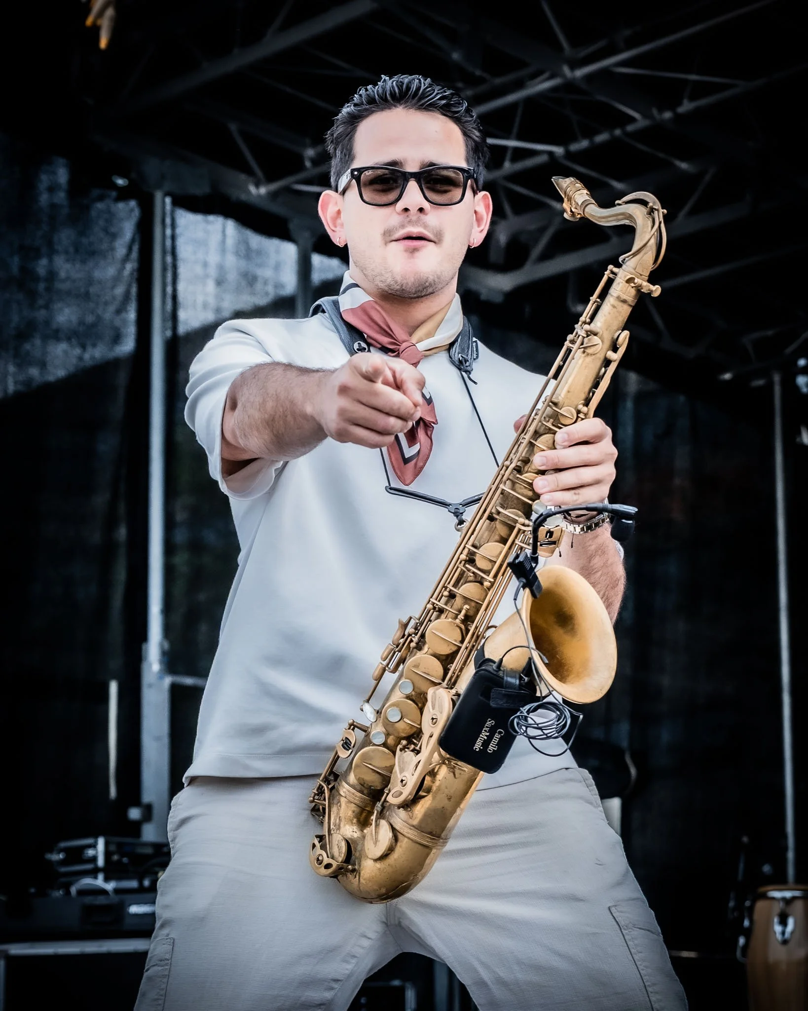 Mannelijke saxofonist speelt op een podium met zwarte achtergrond en metalen structuur.