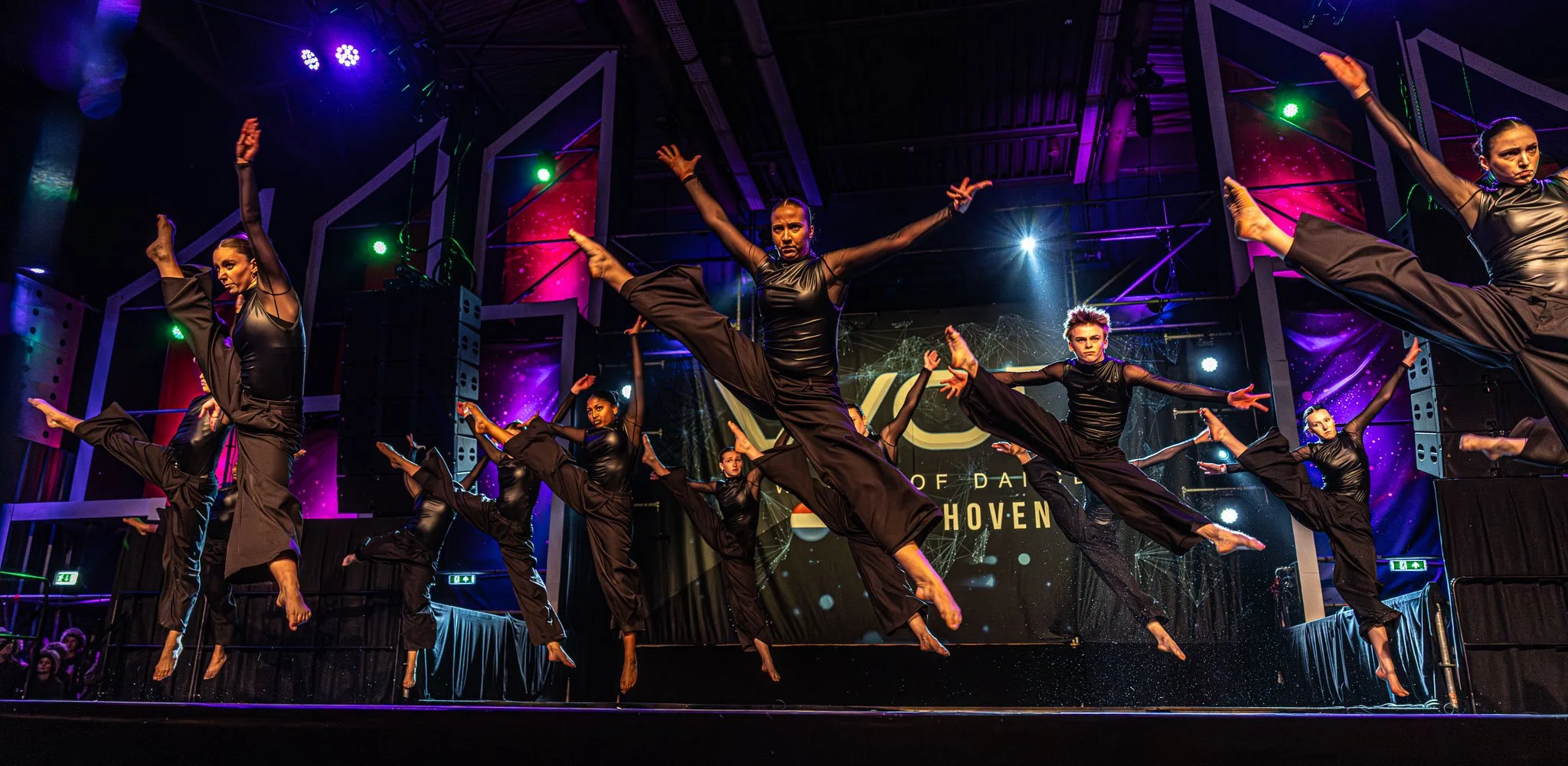 Dames die een choreografie uitvoeren op een podium tijdens een dansshow met kleurrijke lichten.