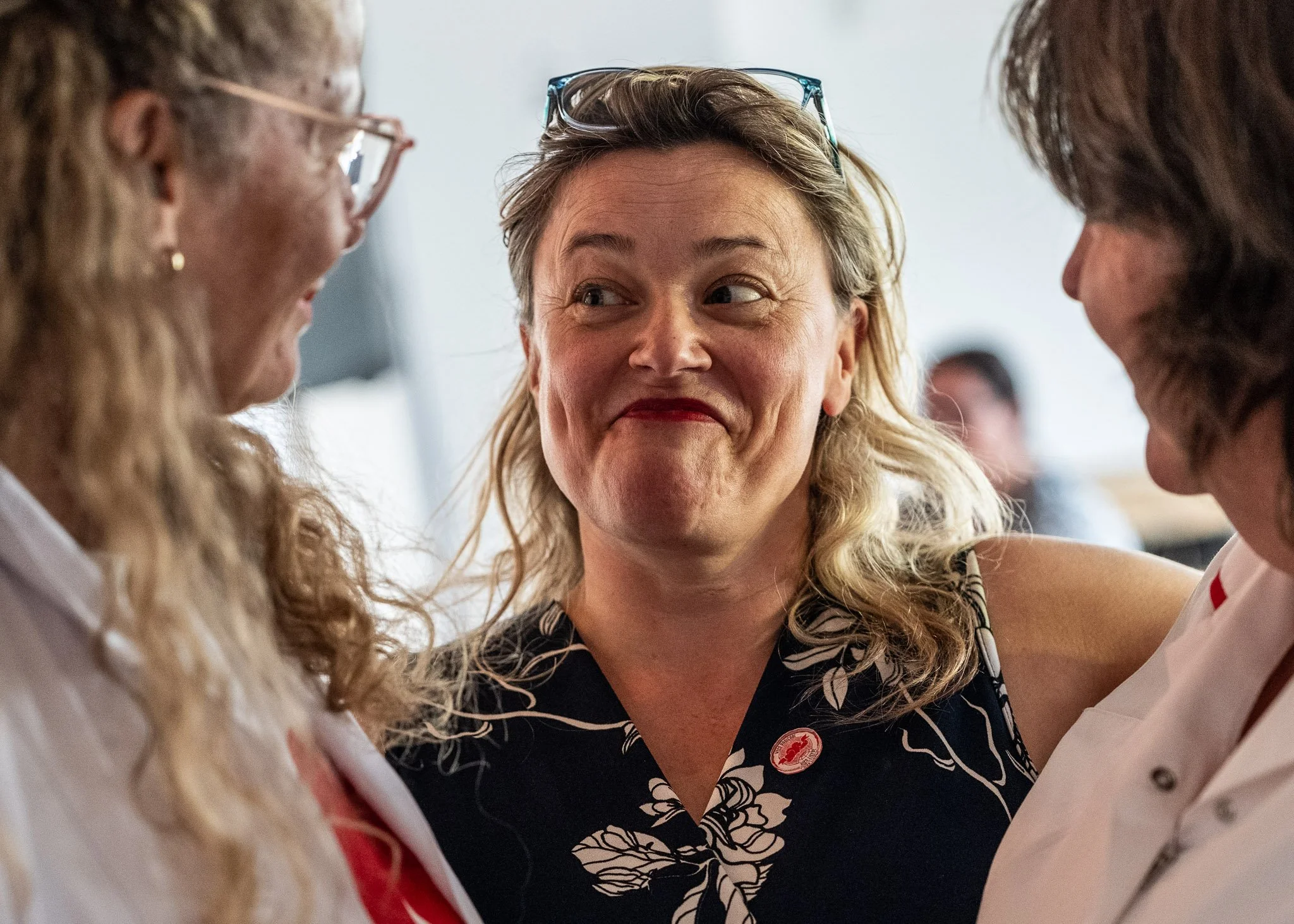 Vrouw die glimlacht en oogcontact maakt met twee andere vrouwen, in een sociale situatie.