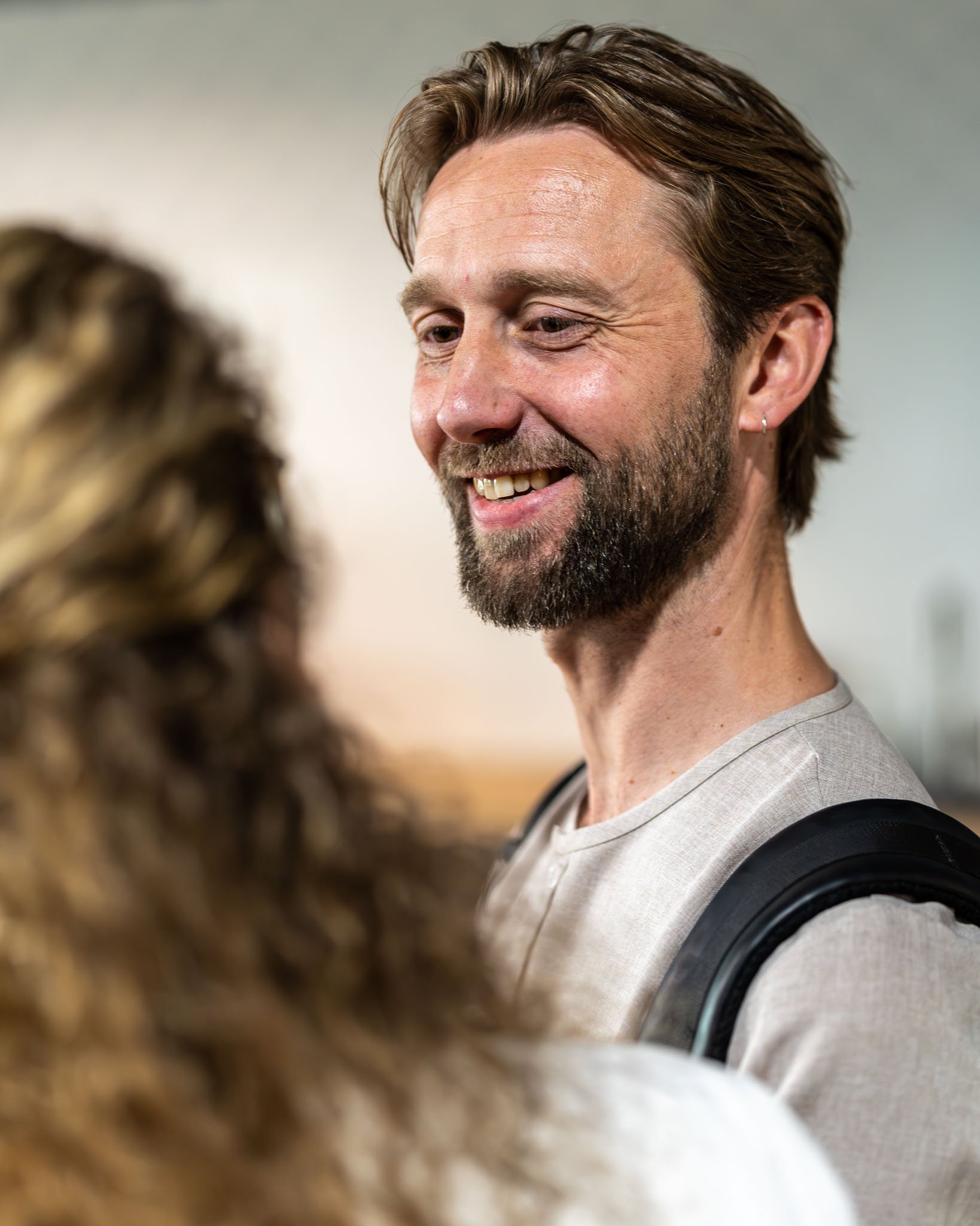 Een glimlachende man met een getrimde baard en haar die naar een kat kijkt, met een achtergrond die niet duidelijk zichtbaar is.
