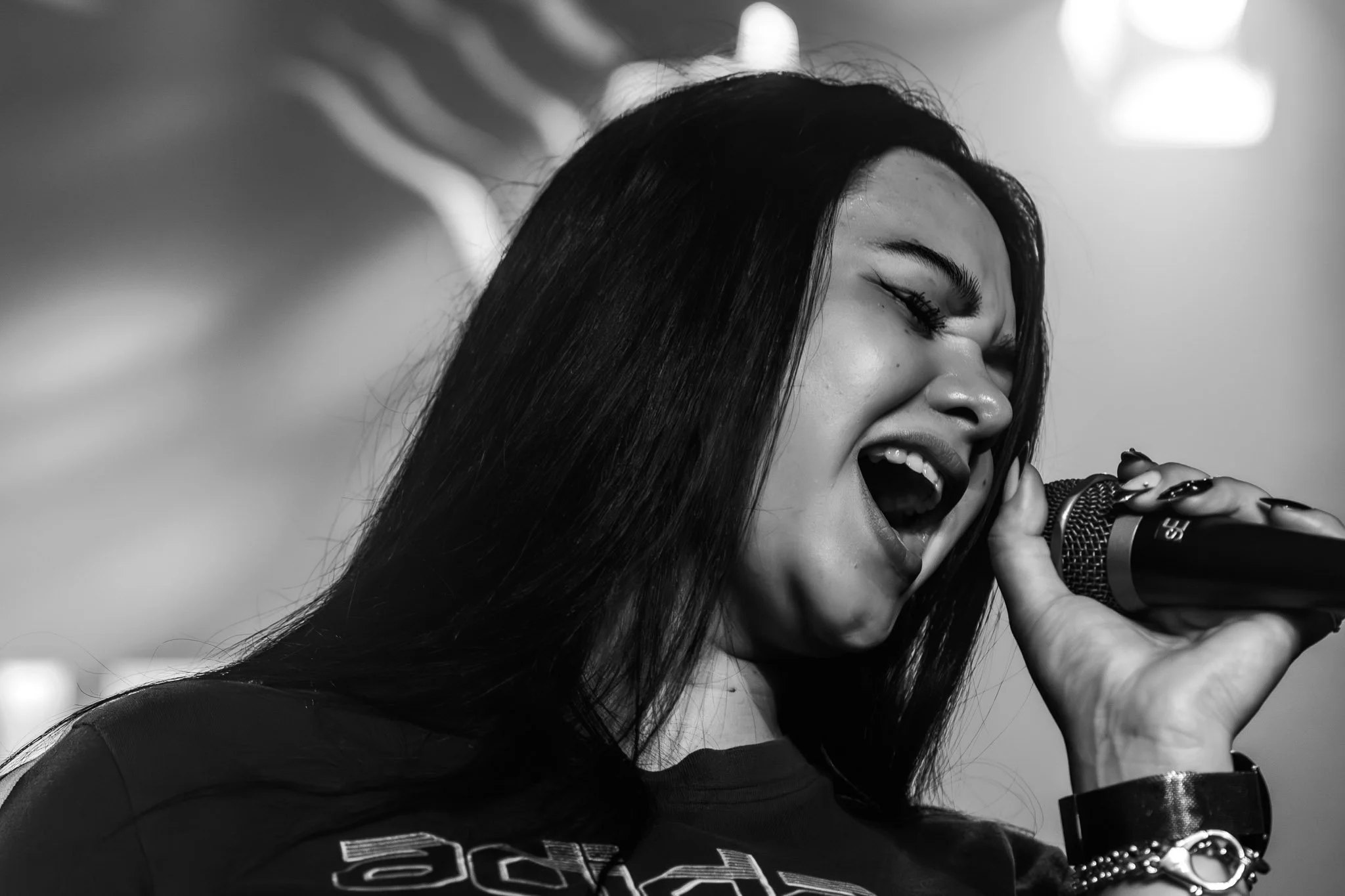 Een vrouw met lang zwart haar zingt in microfoon, haar ogen dicht en glimlachend.