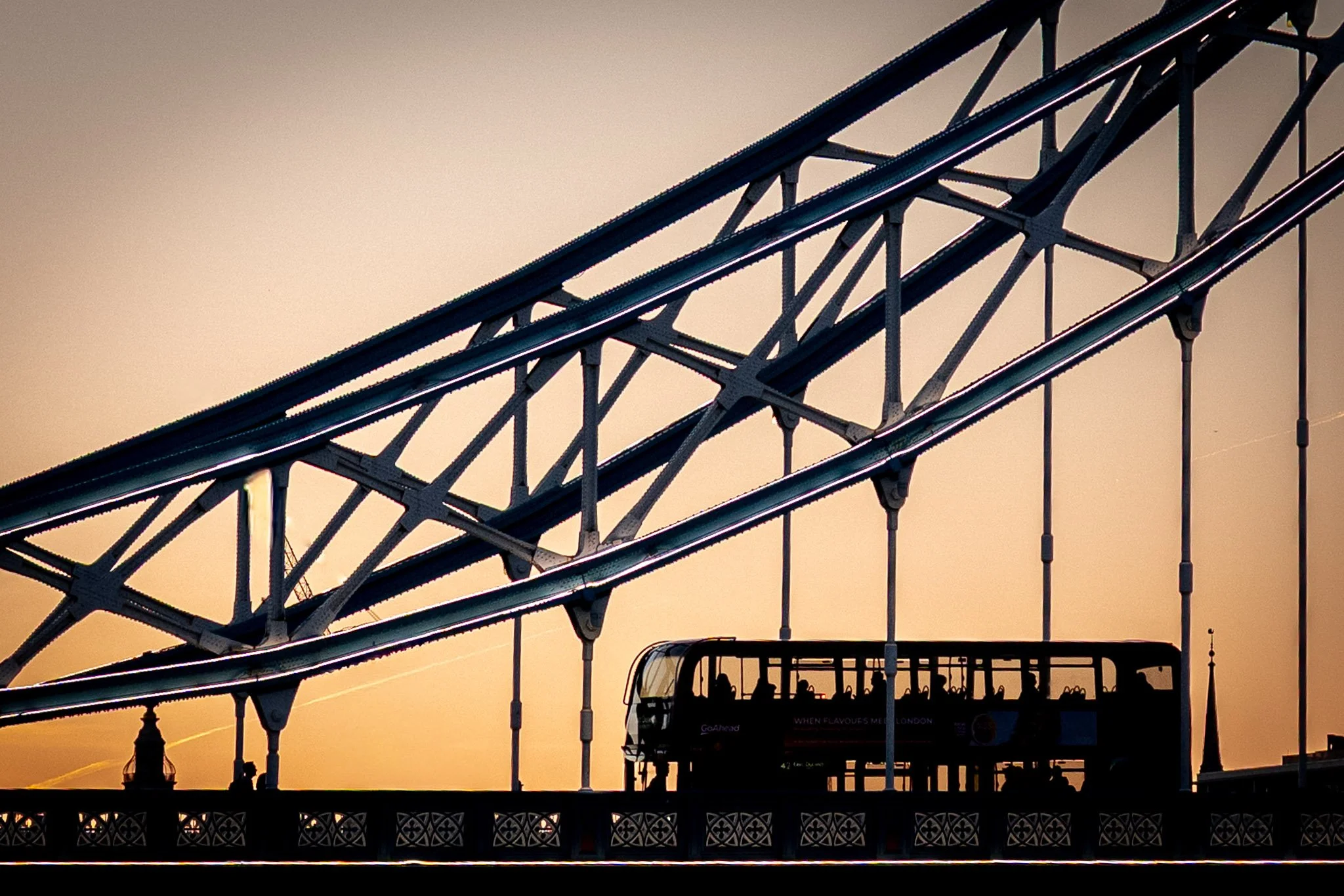 Silhouet van een attractie of treintje met uitzicht op Londen bij zonsondergang, inclusief brug en een dubbeldekker bus.