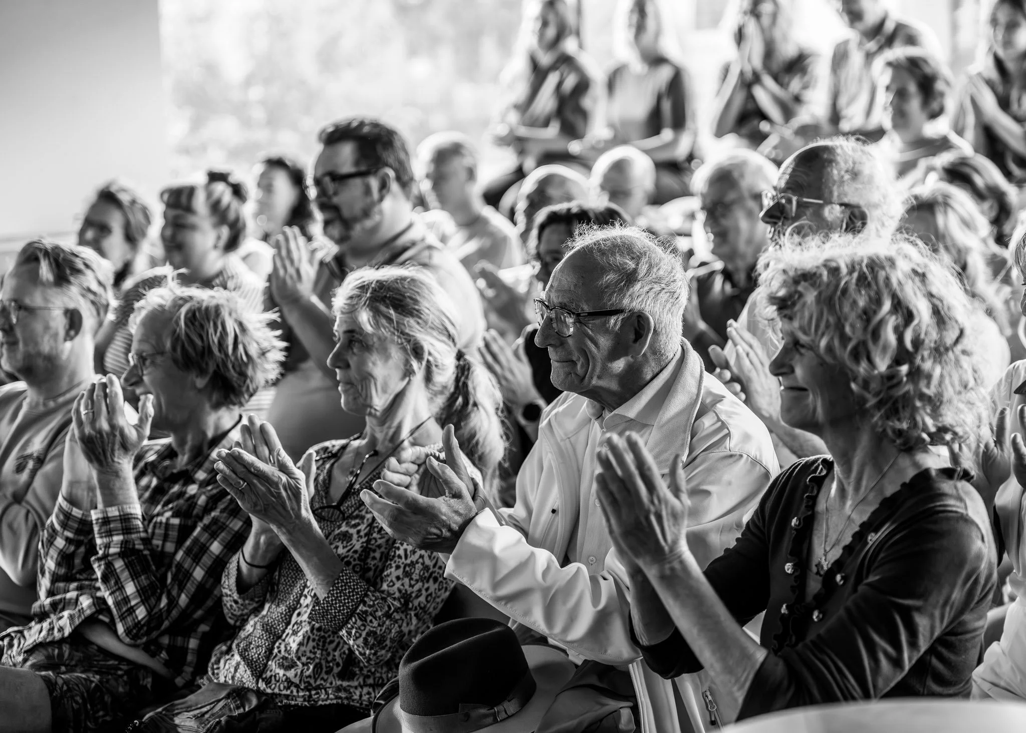 Een groep mensen zittend in een zaal, die mainkelijk ouderen zijn, en met gesloten ogen bidden of mediteren.