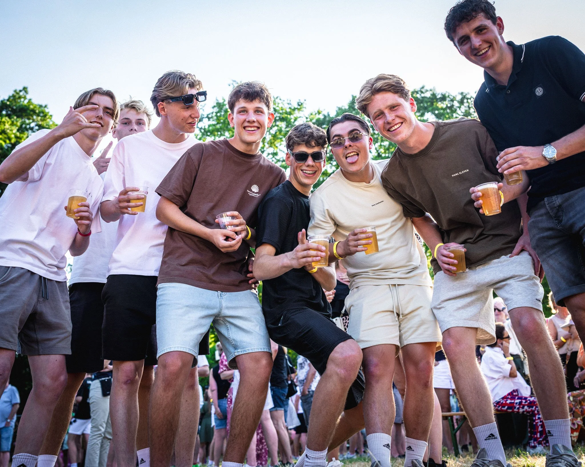 Een groep lachende jongeren die samen in een park staan en drankjes vasthouden, vieren samen.