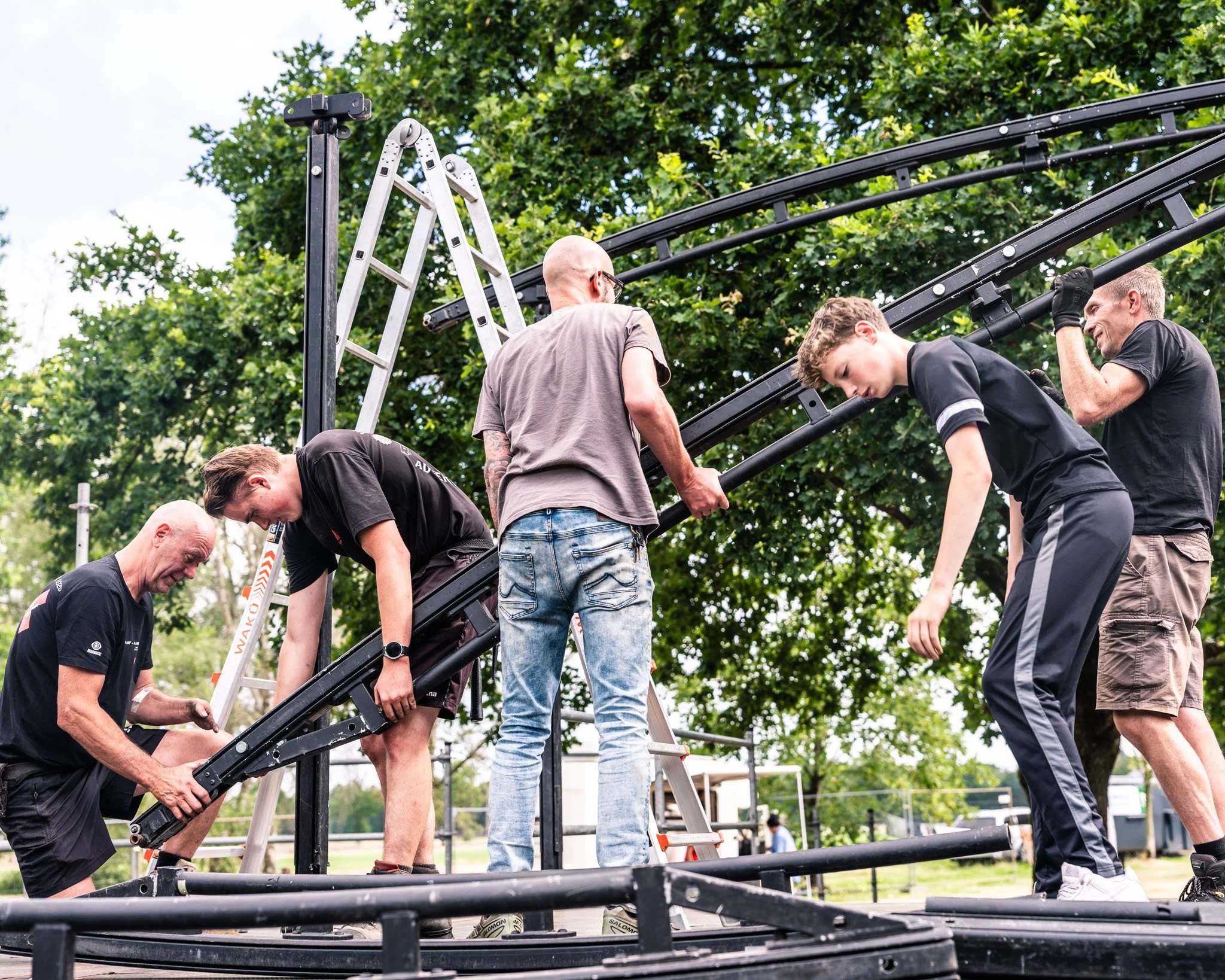 Mensen die een rol proberen te bouwen met een metalen frame, waarbij sommige mensen op een ladder staan en anderen helpen.