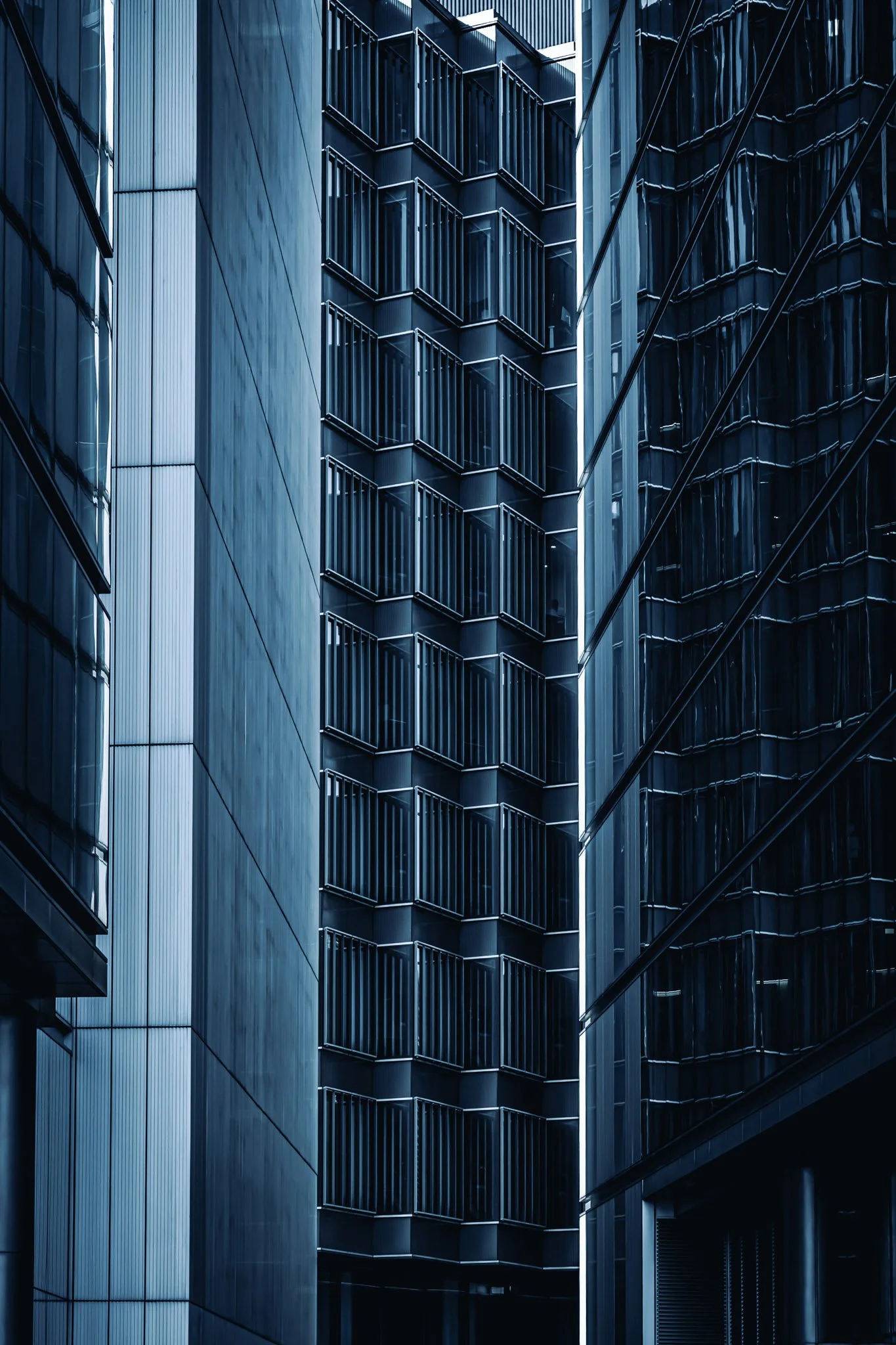 Close-up van een modern hooggebouw met glazen ramen en aluminium gevelpanelen, met een donkerblauwe tint.