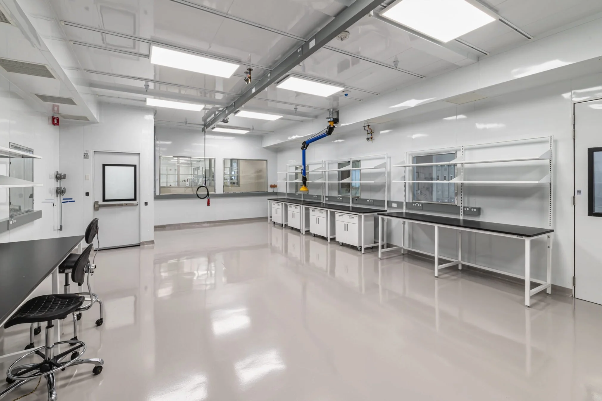 Empty laboratory with white walls, black countertops, shelving, and industrial lighting.