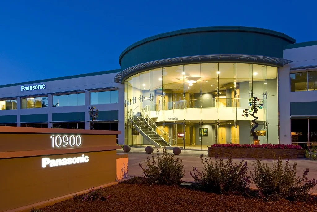 The Panasonic building exterior at dusk with illuminated signage, glass-front entrance, and modern exterior design.