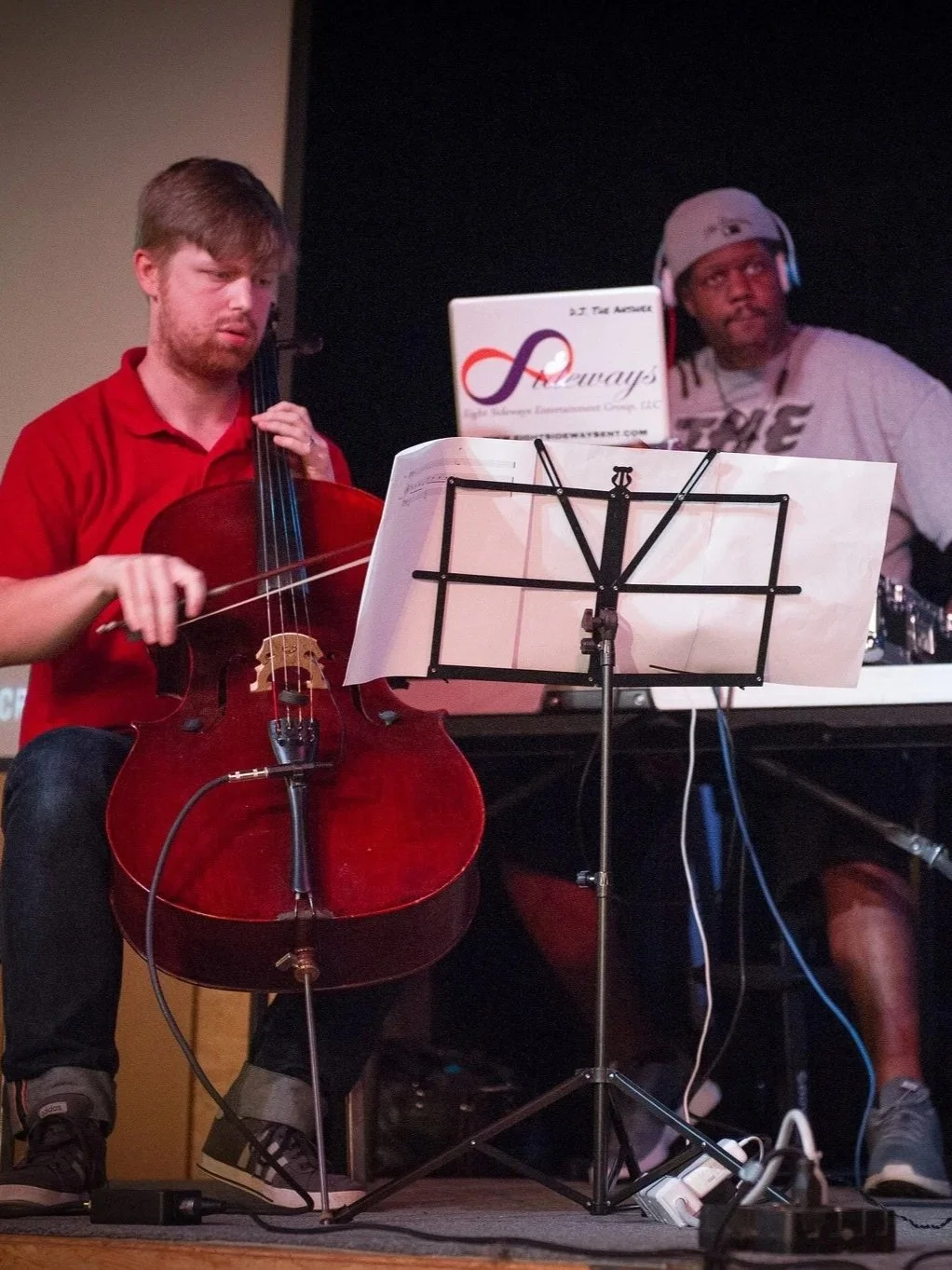 A cellist reads the sheet music as a DJ in the background plays.