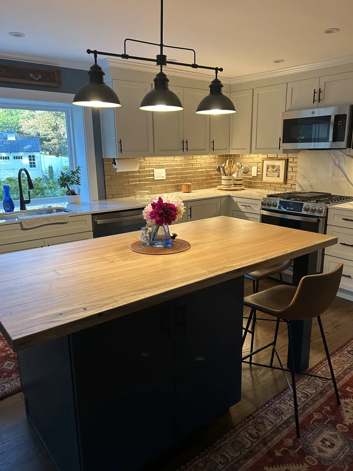 Live edge hardwood island countertop on a navy blue base with black pendant lights and bar stools in a residential kitchen