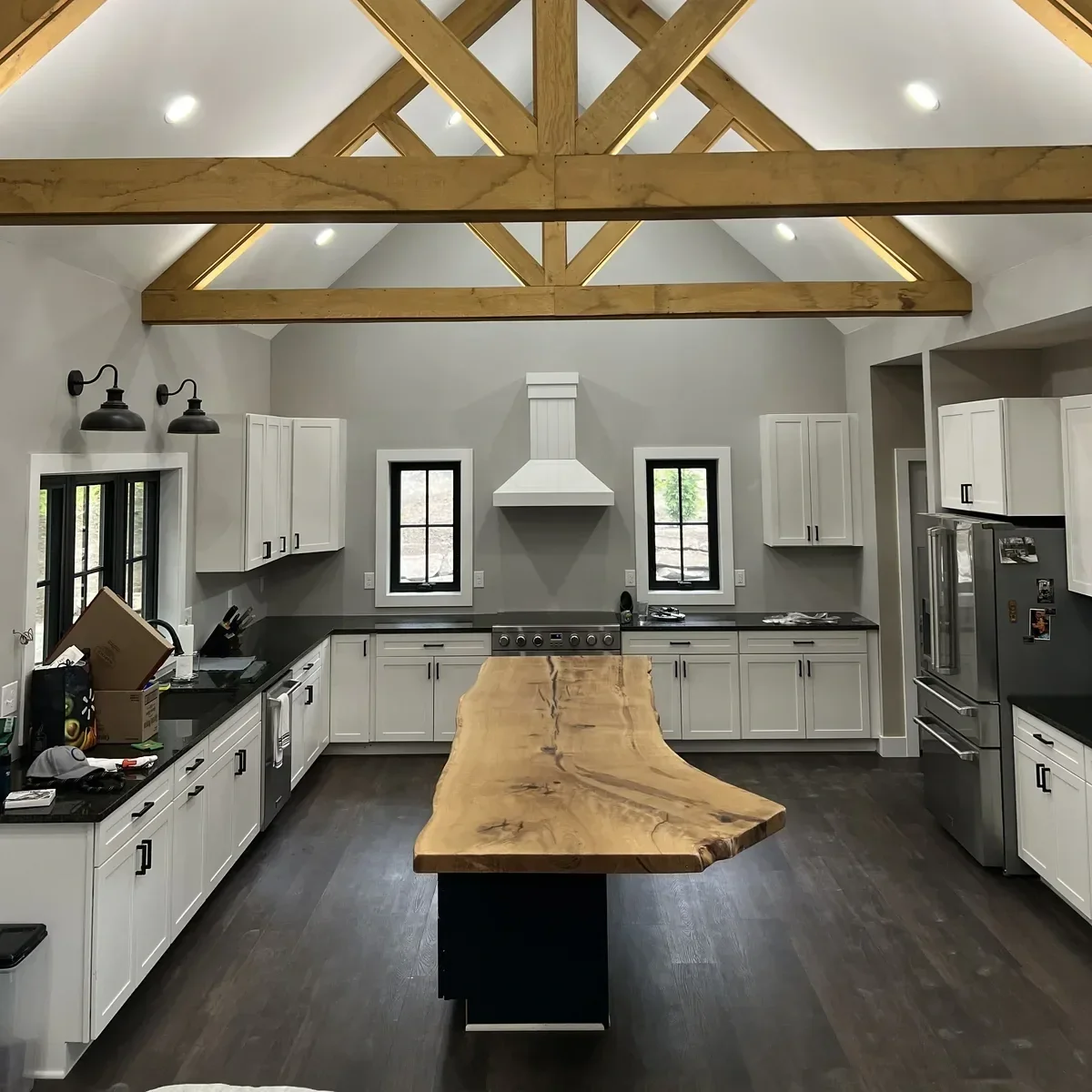 Live edge hardwood kitchen island countertop installed beneath soaring timber-frame trusses — a statement piece in a newly built home