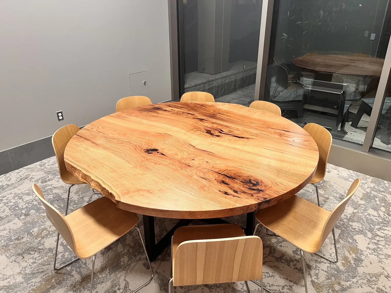 Large custom round live edge table on a black metal base, installed in a modern office setting — seats eight comfortably