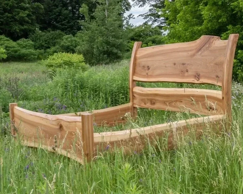 Custom hardwood bed frame with live edge headboard and rails, photographed in a Vermont summer meadow