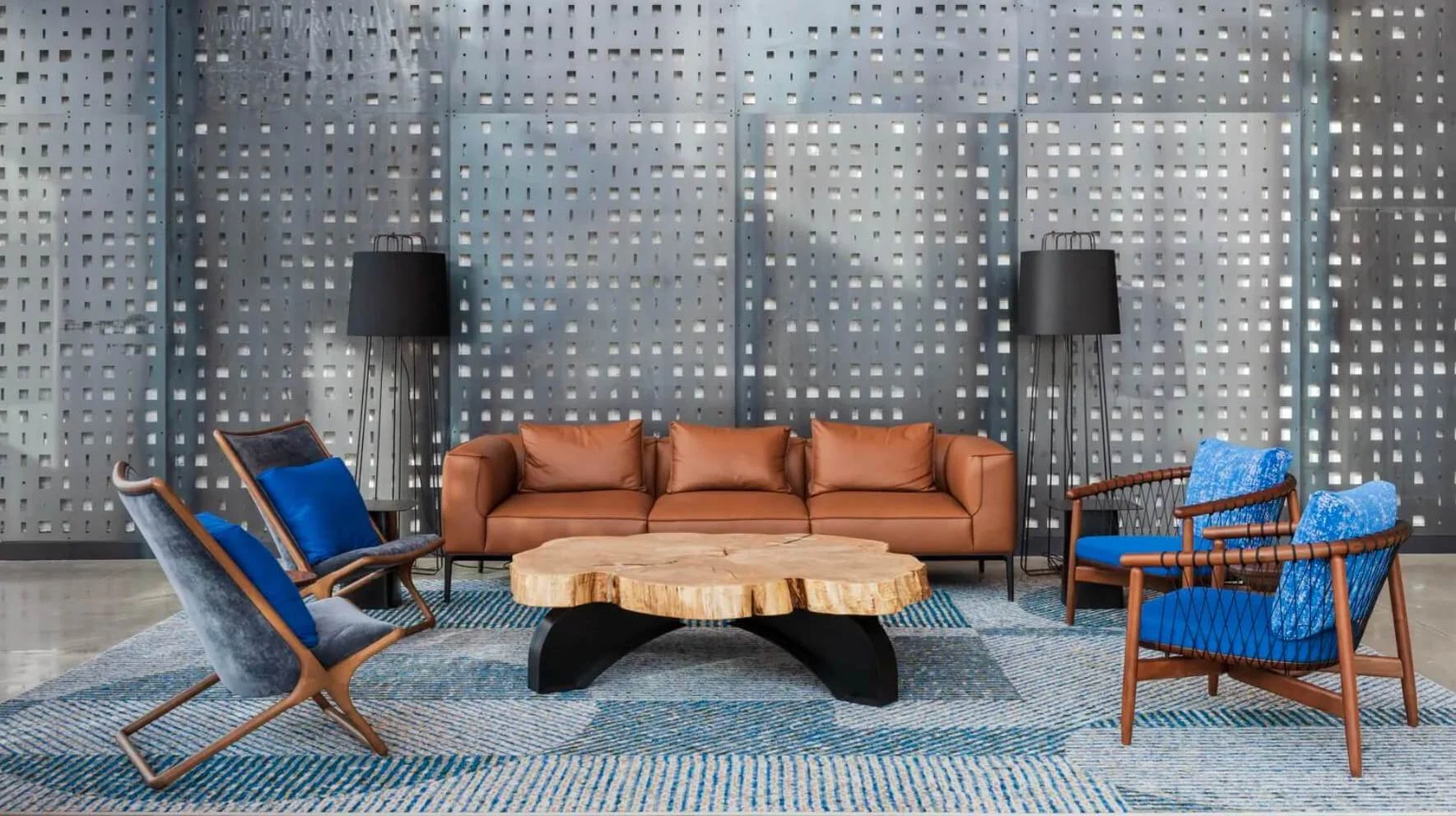 Entry room with a large elm coffee table, a tan sofa and various blue and gray chairs on a striped rug, set against a perforated gray wall at Boston Dynamics