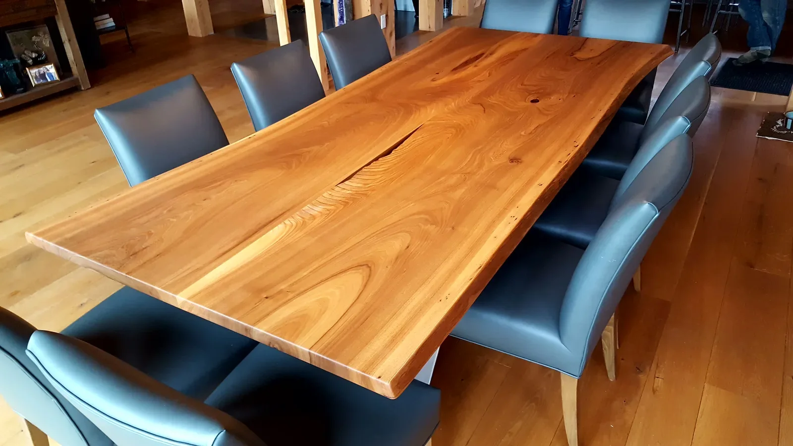 Large live edge dining and conference table with blue leather chairs, installed in a timber-frame home