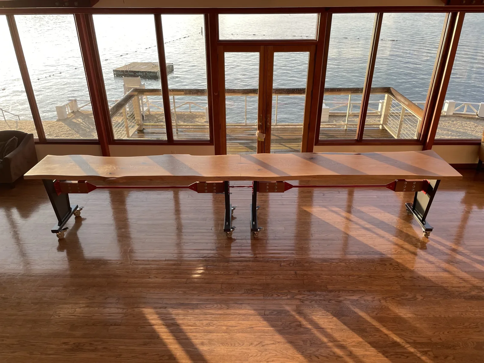 Extra-long live edge bar table on industrial adjustable-height legs with casters, installed in a waterfront venue with lake views