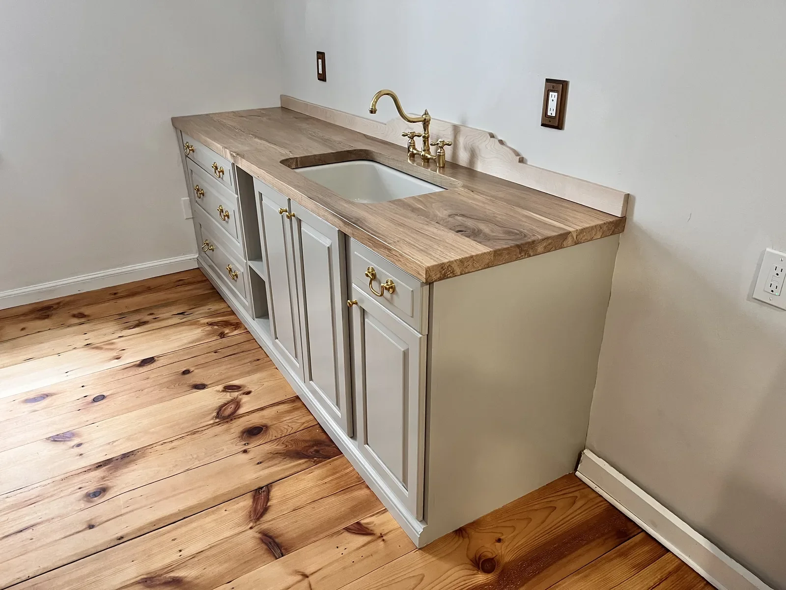Live edge hardwood countertop on a painted vanity with farmhouse sink and brass fixtures, installed in a cottage-style home