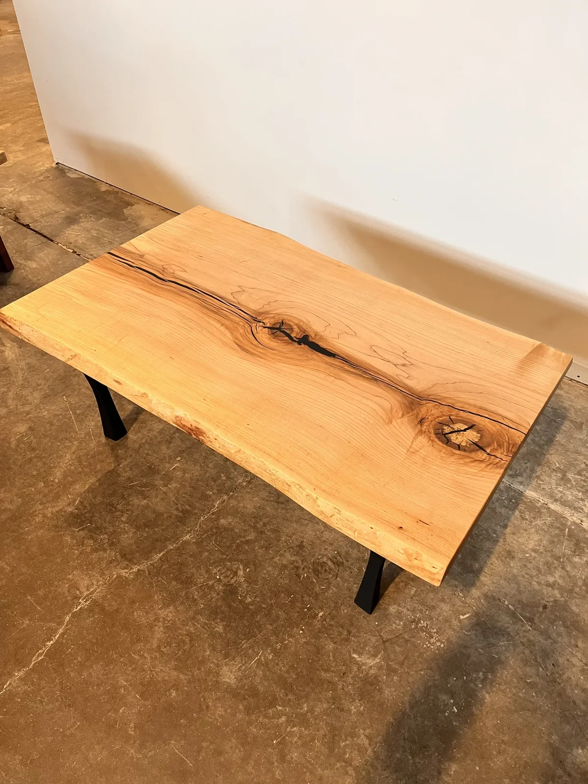Live edge coffee table with dramatic knots and natural cracks, on black metal legs — showcasing the character of salvaged hardwood
