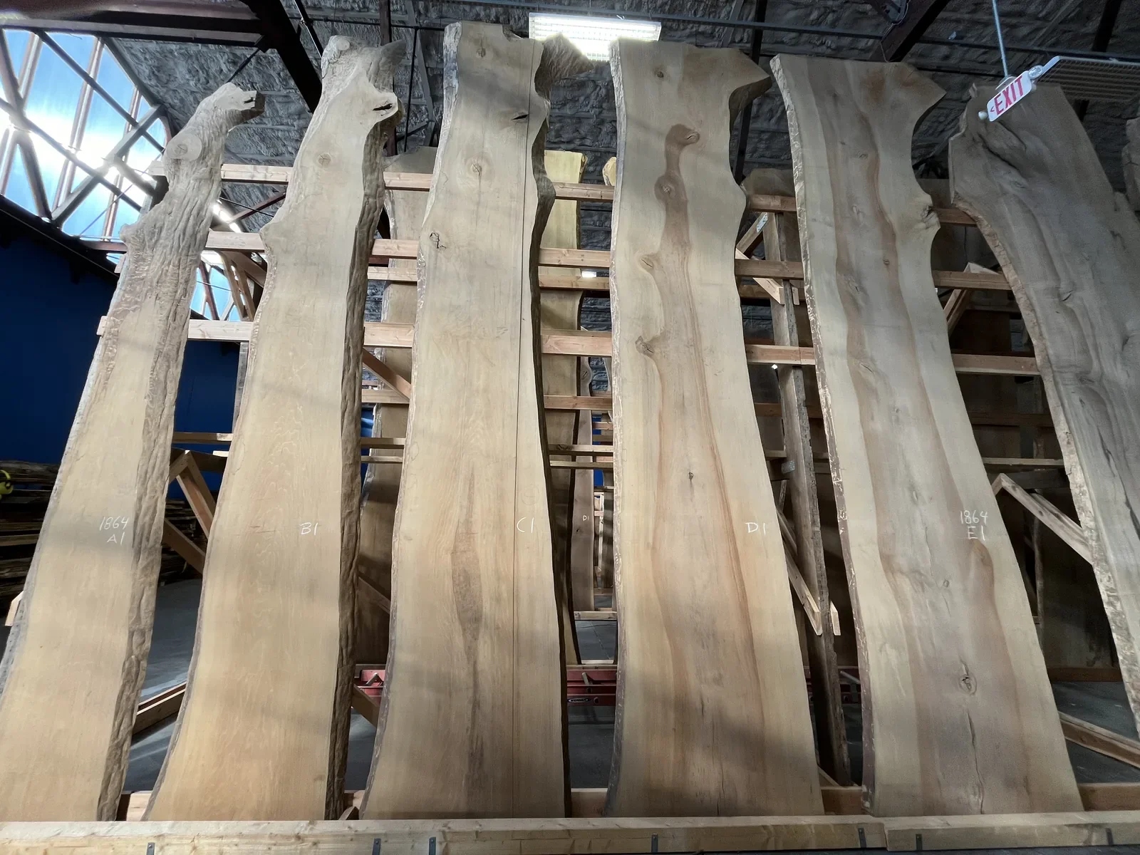 Large slabs of raw wood with natural edges, stored vertically on wooden storage racks inside a warehouse or workshop.