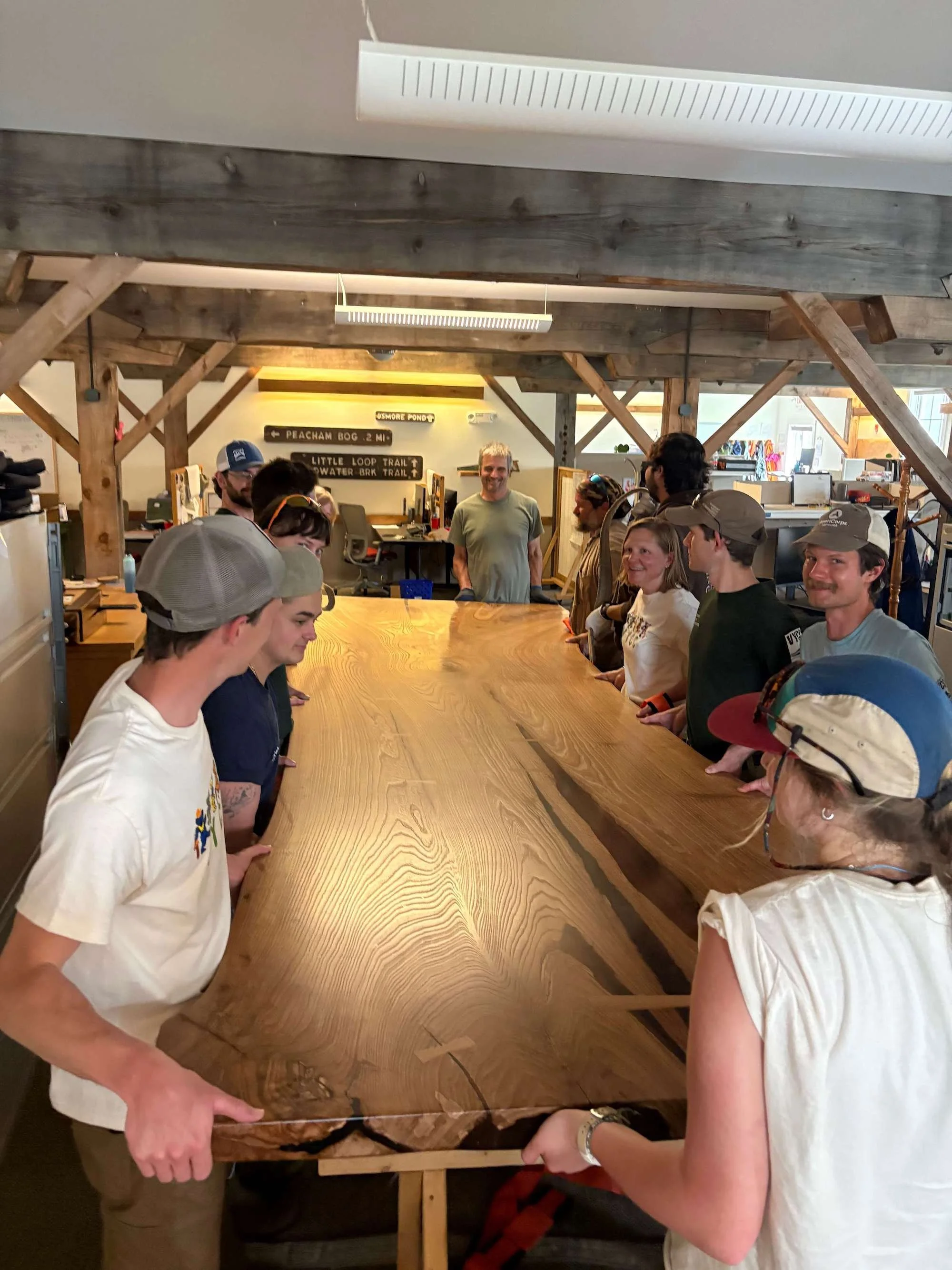 People at Vermont Youth Conservation Corps working together to move a large Red Elm wooden table their indoor gathering space.